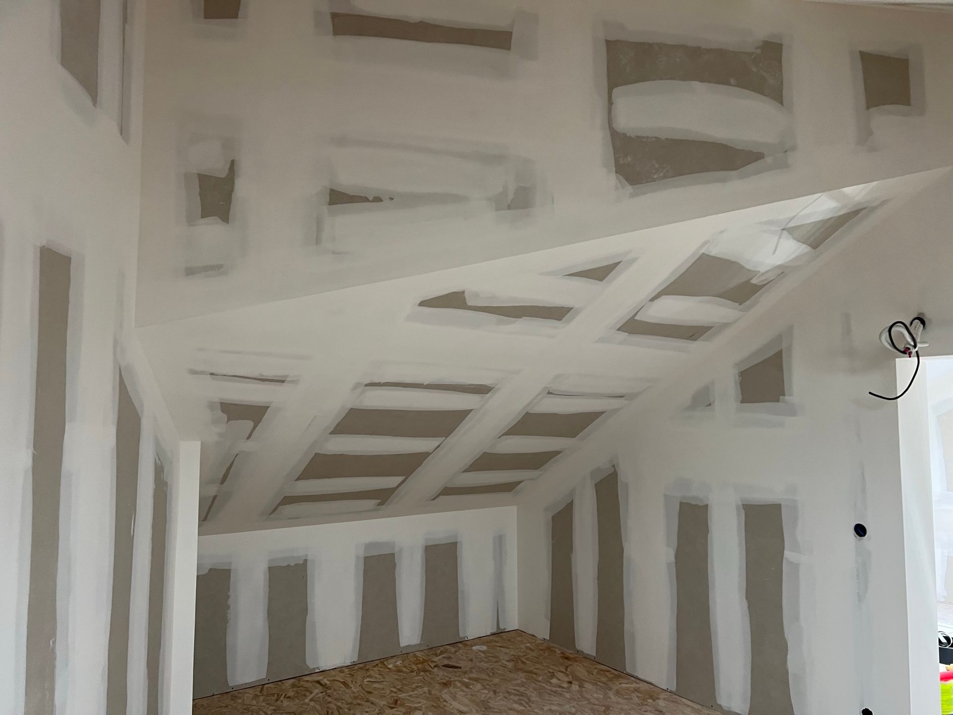 Intérieur avec plaques de plâtre, ruban et enduit, montrant un plafond et des murs en pente partiellement construits.
