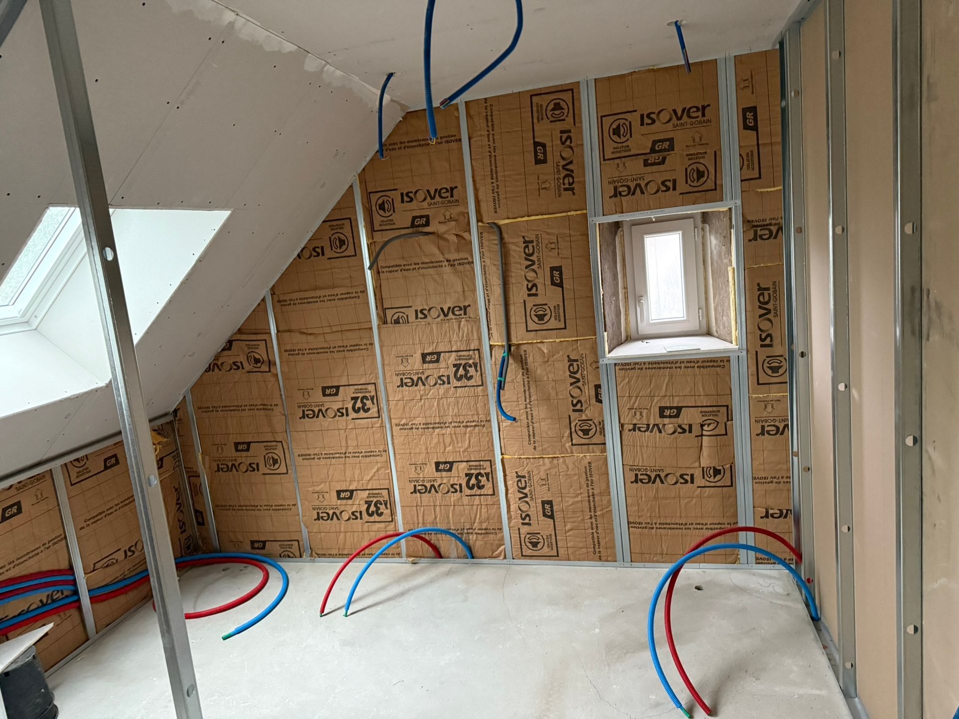 Aménagement intérieur : murs isolés, ossature métallique, tuyauterie, petite fenêtre, plafond mansardé.