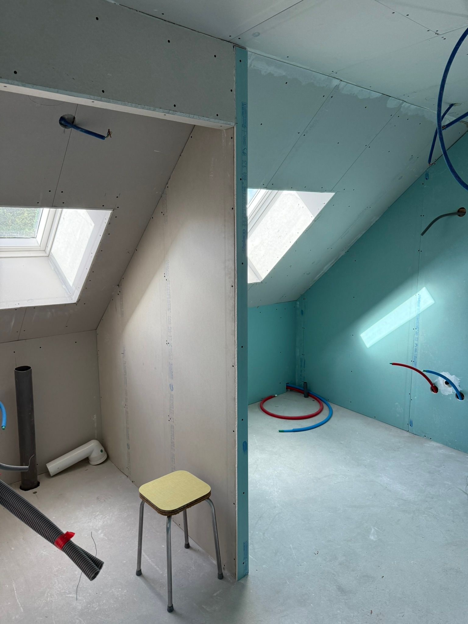 Pièces intérieures en cours d'aménagement, avec cloisons sèches, puits de lumière, plomberie et un petit tabouret.