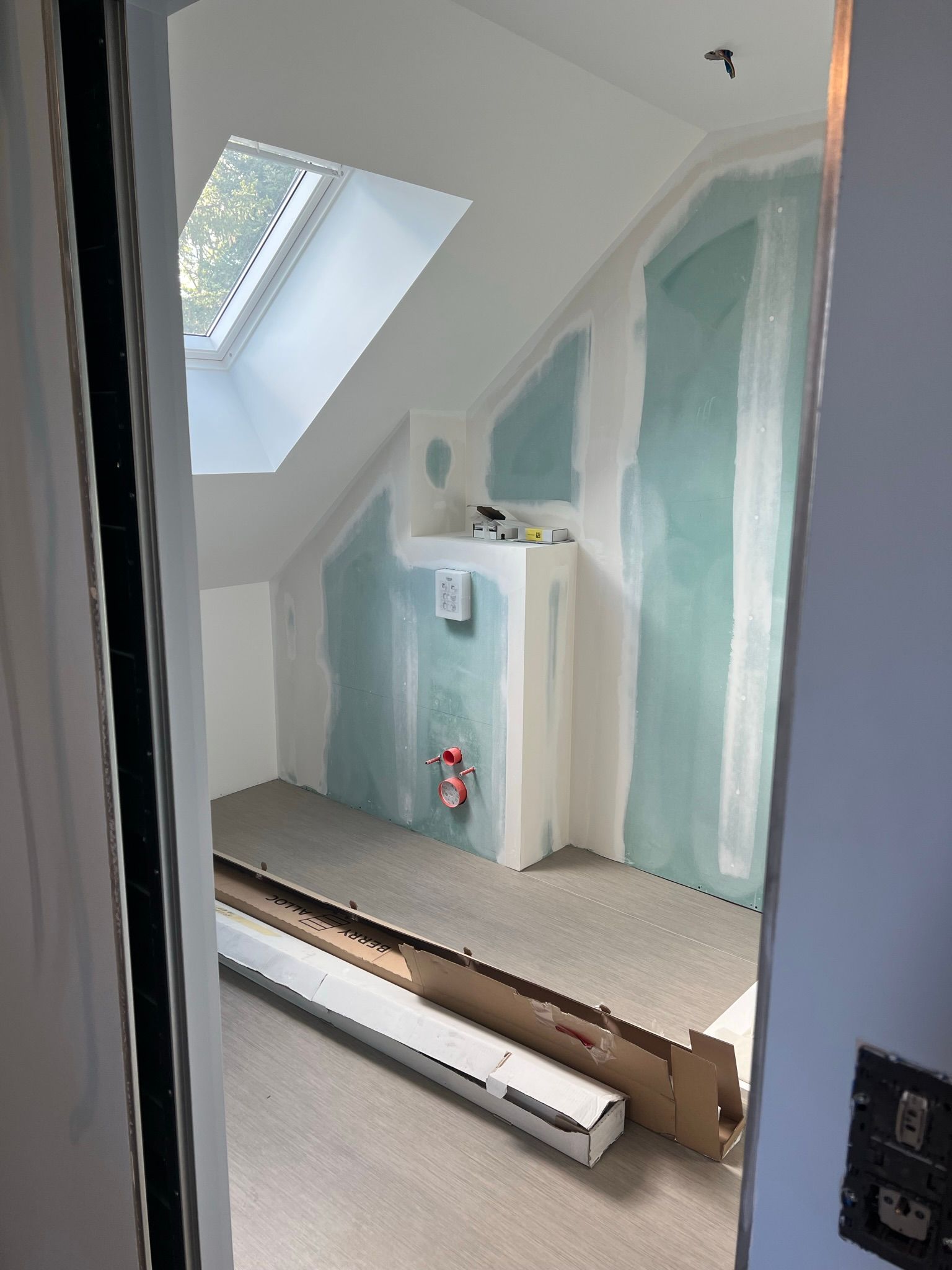 Intérieur d'une pièce en construction, avec cloisons sèches, puits de lumière et matériaux au sol.