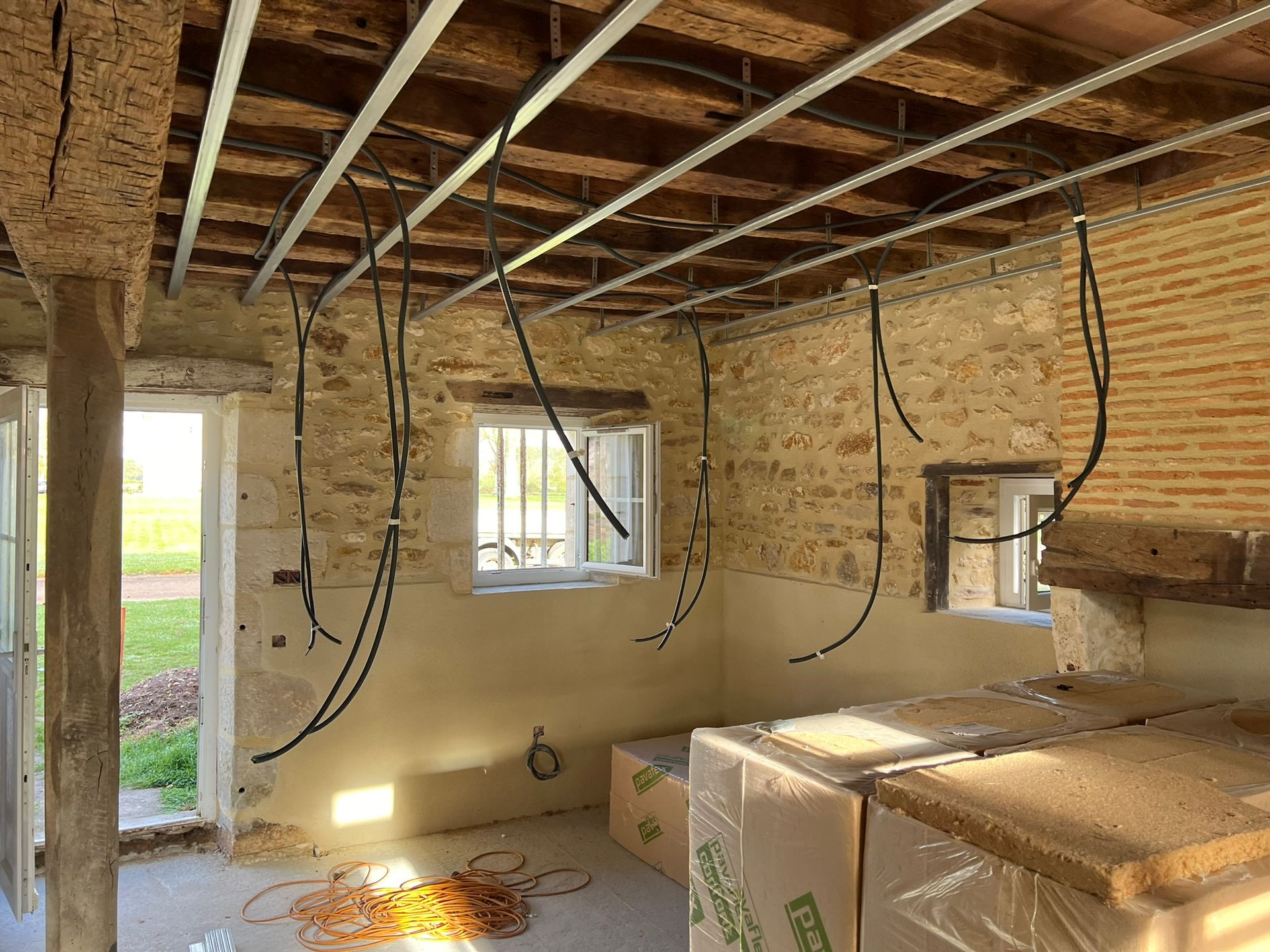 Intérieur d'une pièce en construction avec murs en pierre apparente, câbles électriques et ossature de plafond.