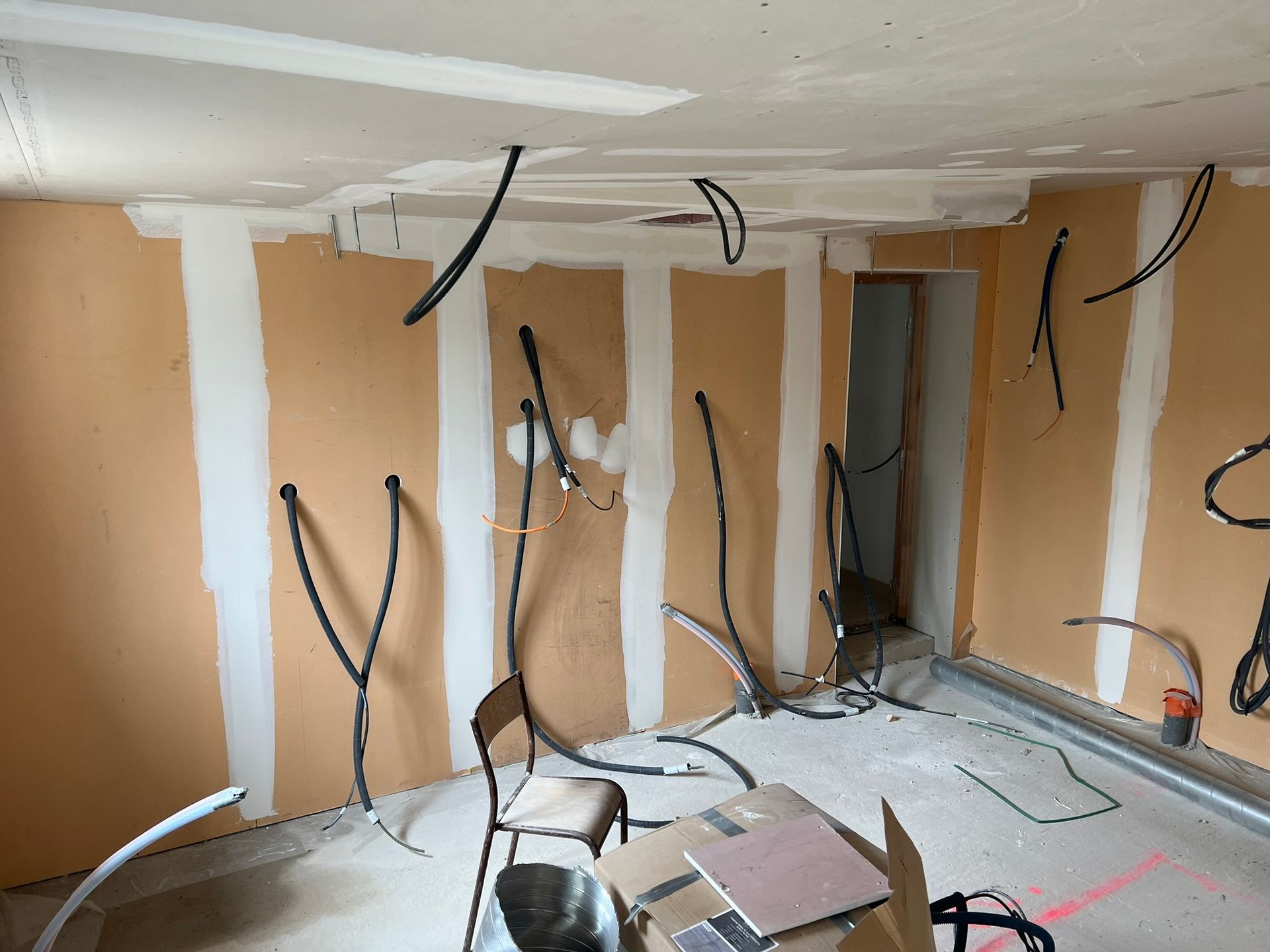 Pièce intérieure en travaux, fils électriques apparents, plaques de plâtre partiellement posées sur les murs et le plafond.