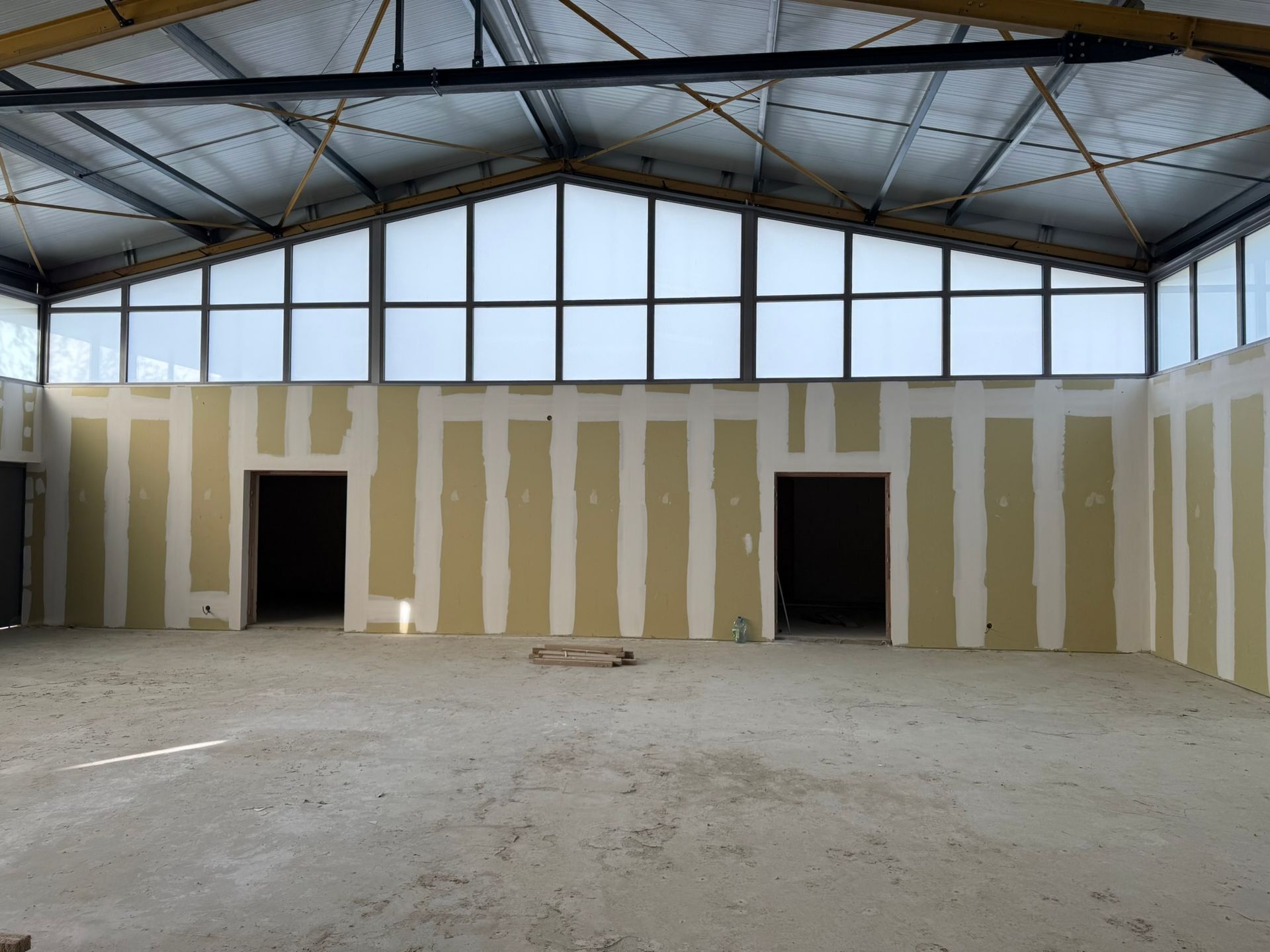 Grand bâtiment inachevé avec sol en béton, murs en plaques de plâtre et puits de lumière.