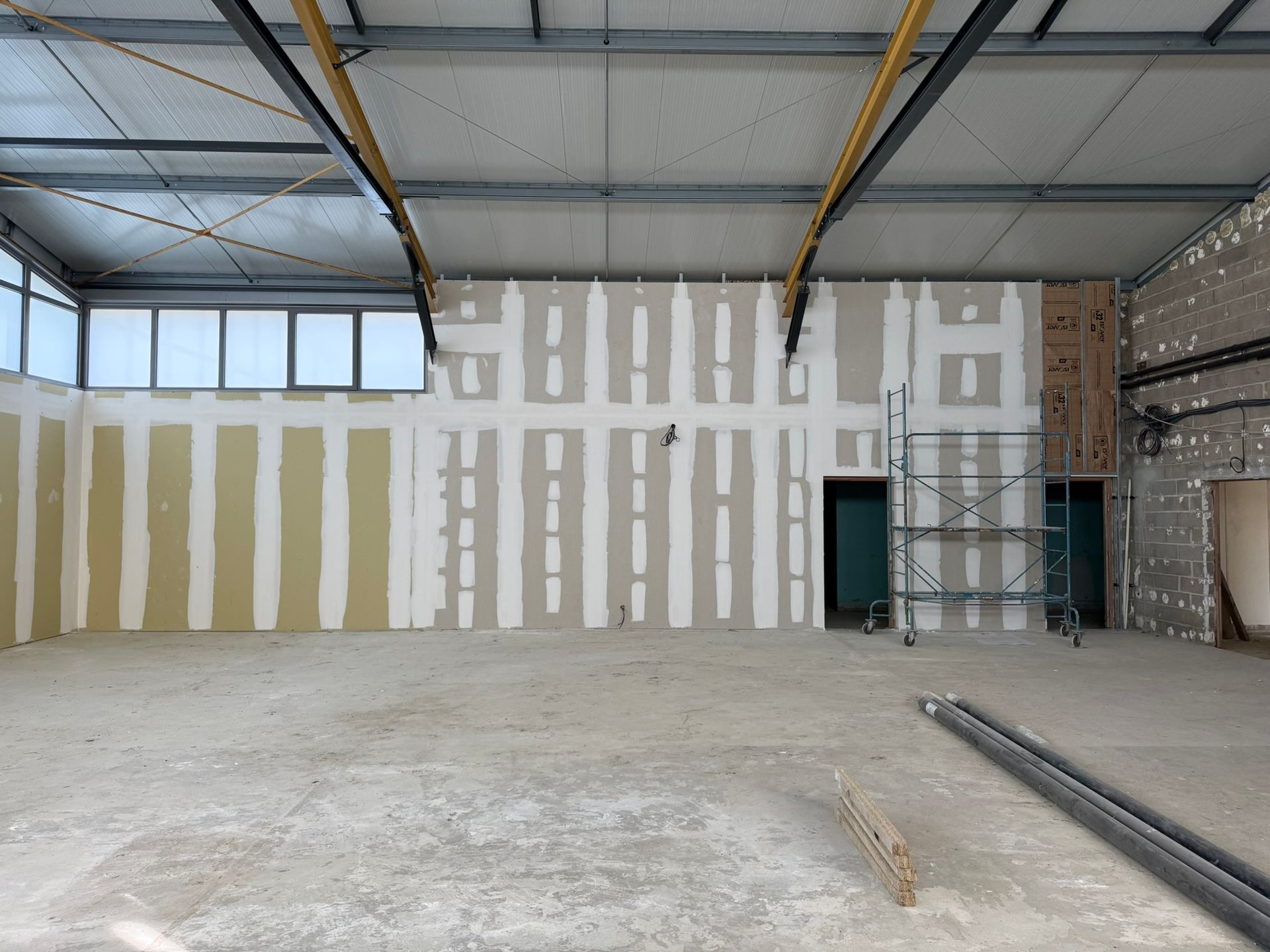 Intérieur d'un bâtiment en construction : murs isolés, échafaudage et sol en béton brut.