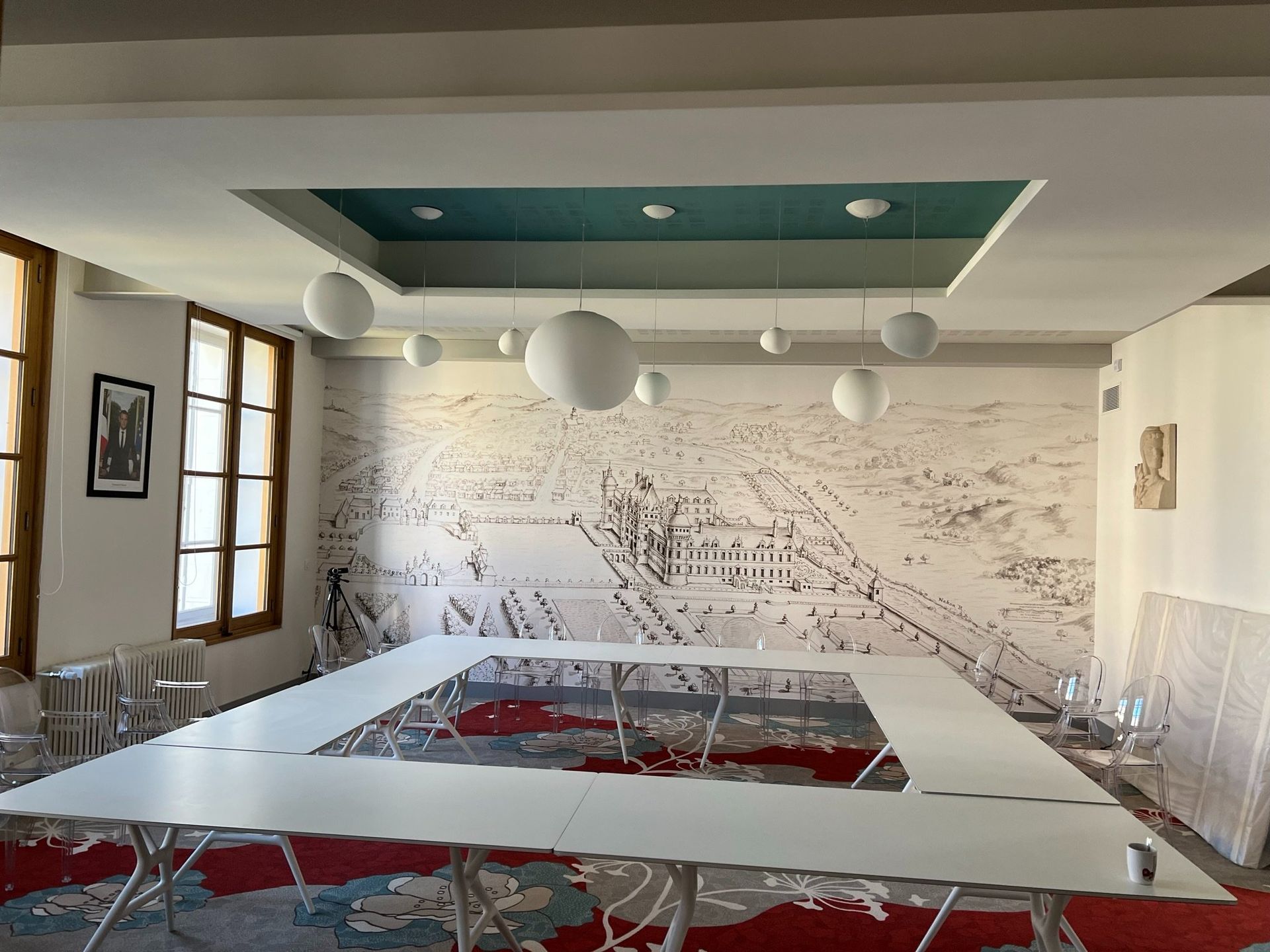 Salle de conférences avec une grande table carrée, des murs blancs et des luminaires sphériques.
