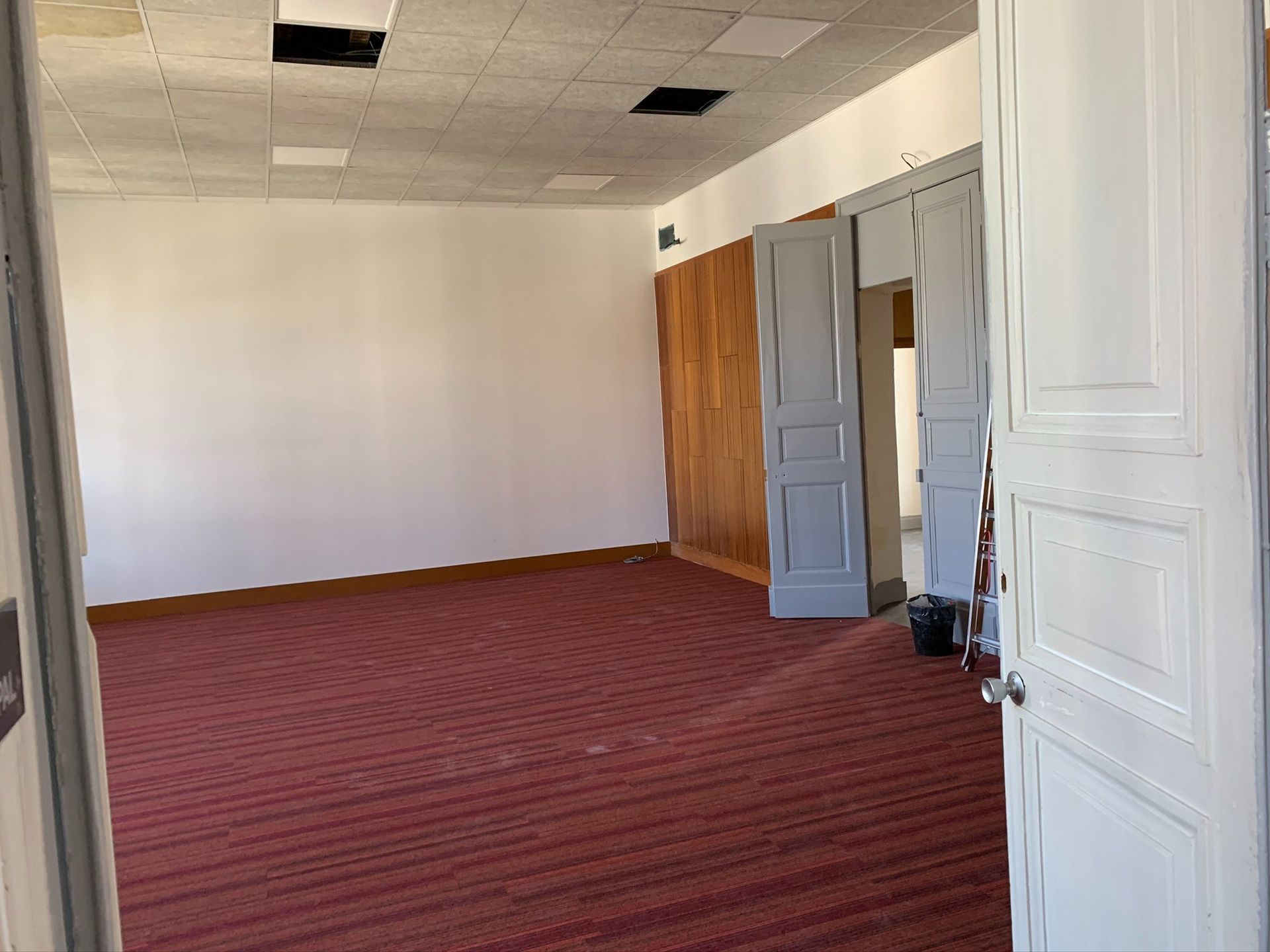 Pièce vide avec moquette rouge, murs blancs et portes ouvertes.