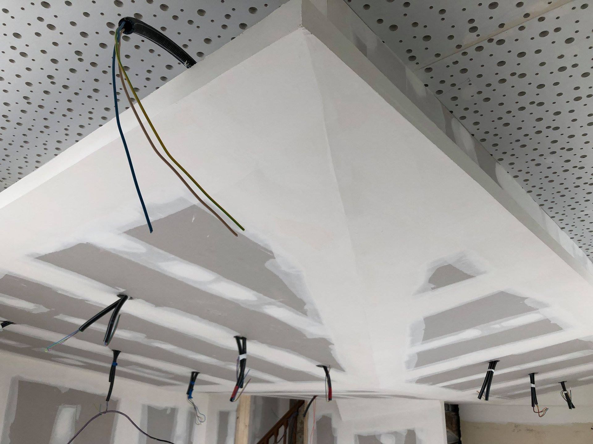 Coin de plafond en plaques de plâtre blanches avec fils électriques apparents, construction inachevée.