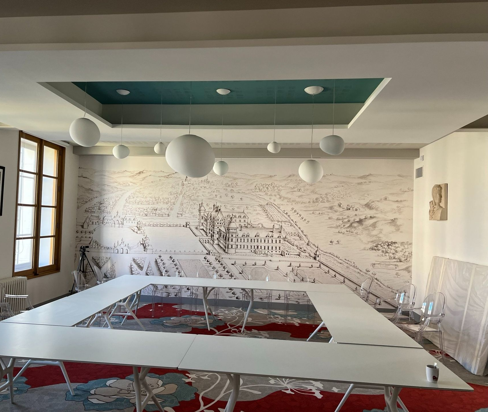 Salle de conférences avec une grande table carrée, des murs blancs et des suspensions lumineuses en forme de globe.