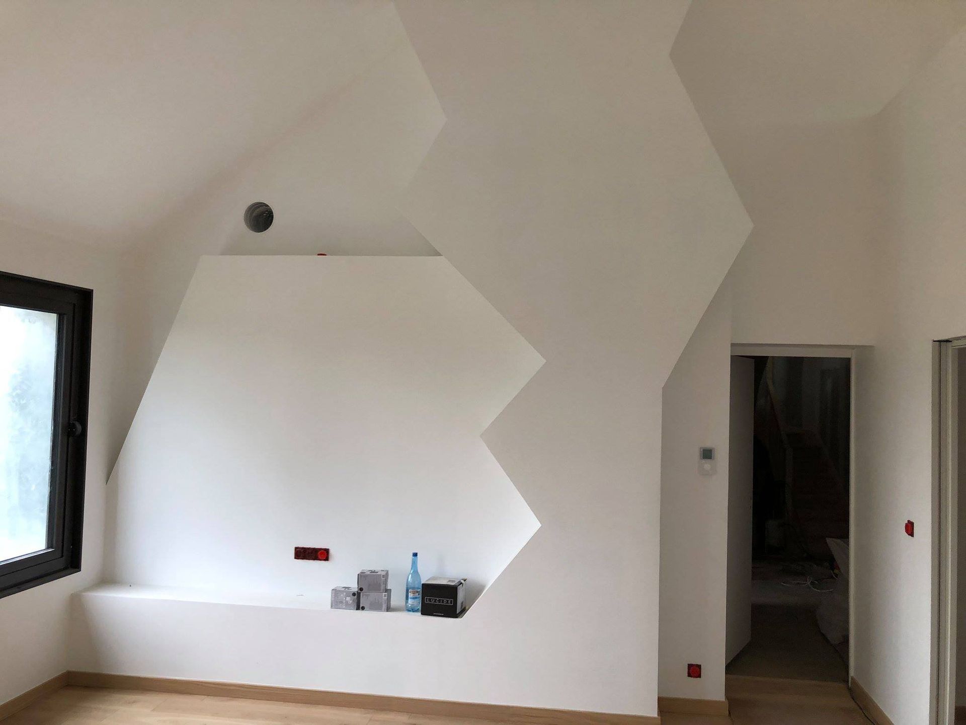 Intérieur avec murs blancs, design géométrique, fenêtre, porte et parquet clair.