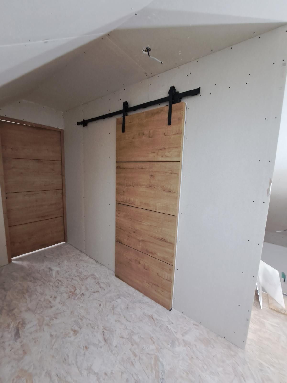 Porte coulissante de grange et porte en bois dans une pièce aux murs blancs et au sol clair.