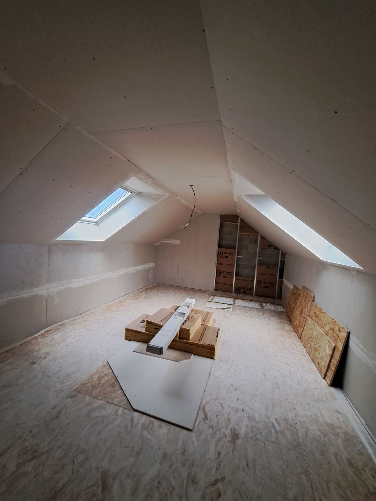 Aménagement d'une pièce sous les combles avec puits de lumière, cloisons sèches, poutres en bois et plancher en contreplaqué.