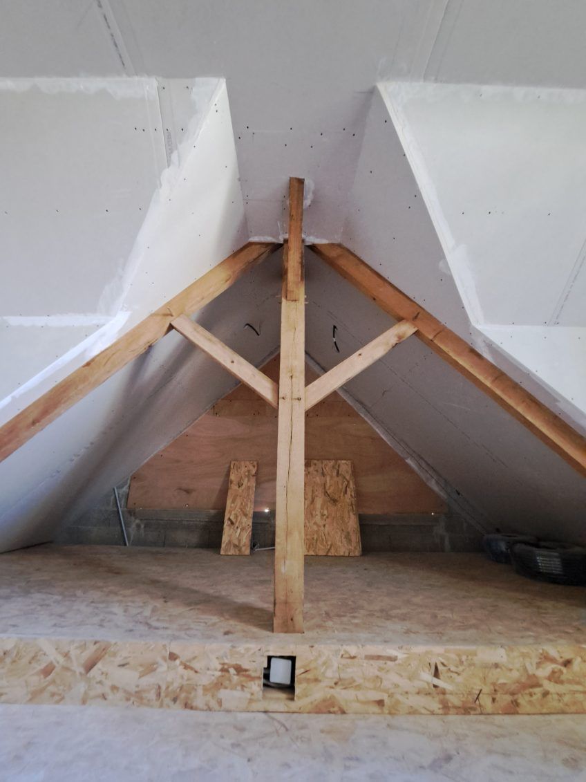 Vue intérieure d'un grenier non aménagé avec des supports en bois et des cloisons sèches.