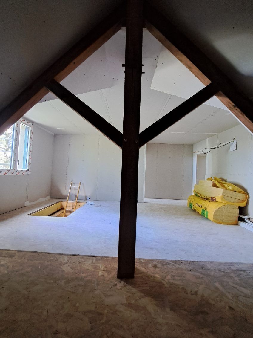 Intérieur d'un grenier non aménagé avec poutres apparentes et un poteau de soutien.