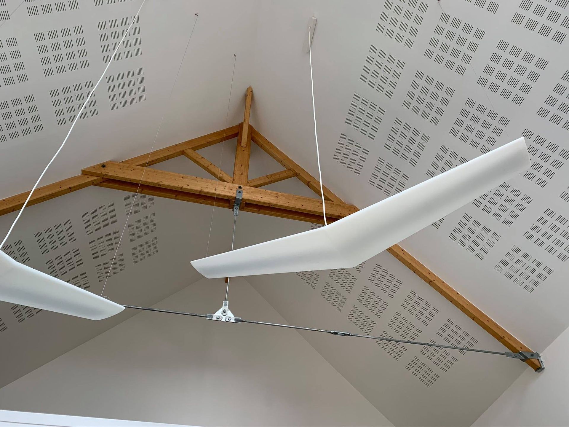 Panneaux acoustiques blancs et structures suspendues dans une pièce à charpente apparente en bois.