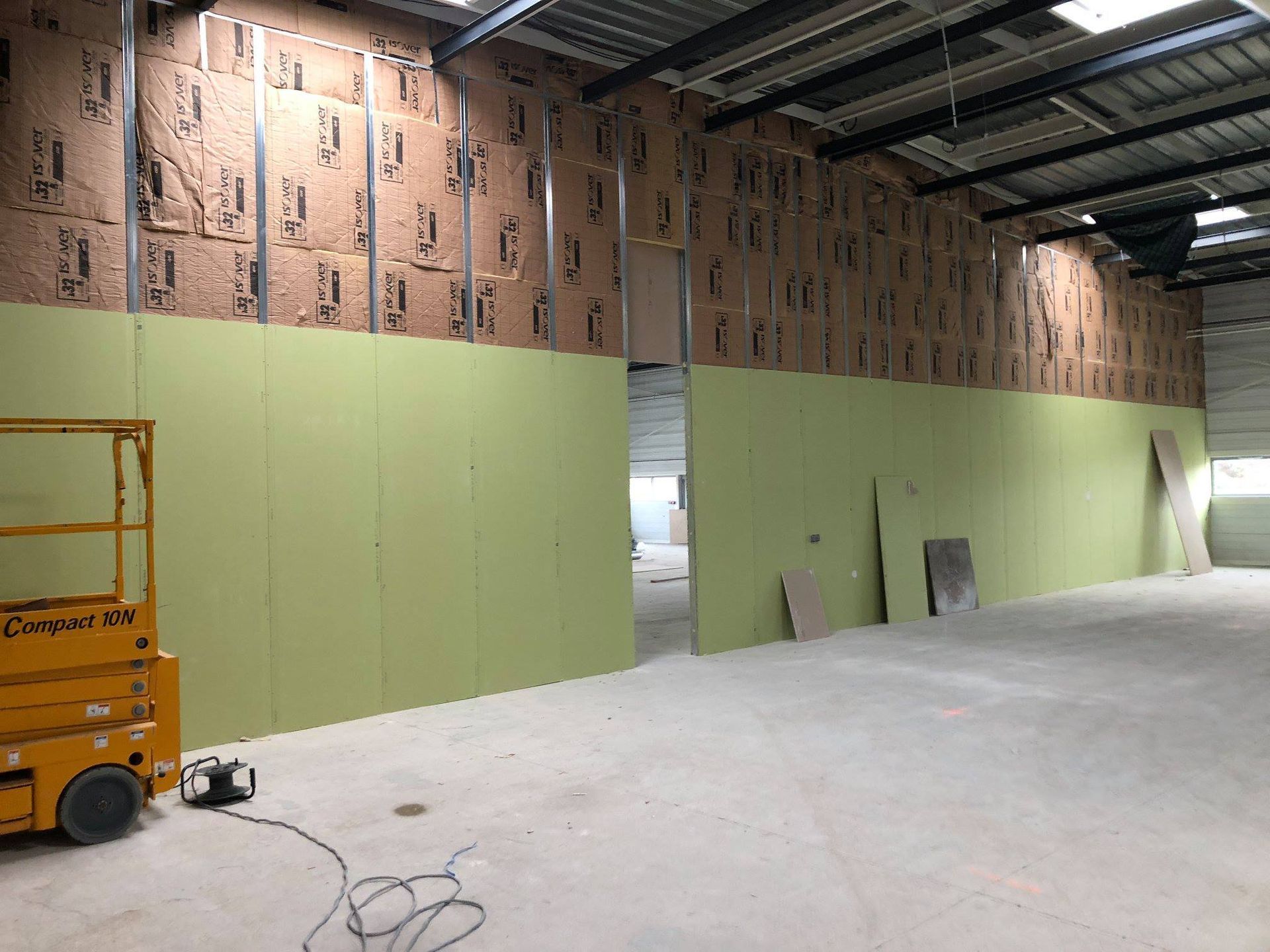 Intérieur d'un bâtiment en construction. Les murs sont recouverts de panneaux verts et d'isolant.