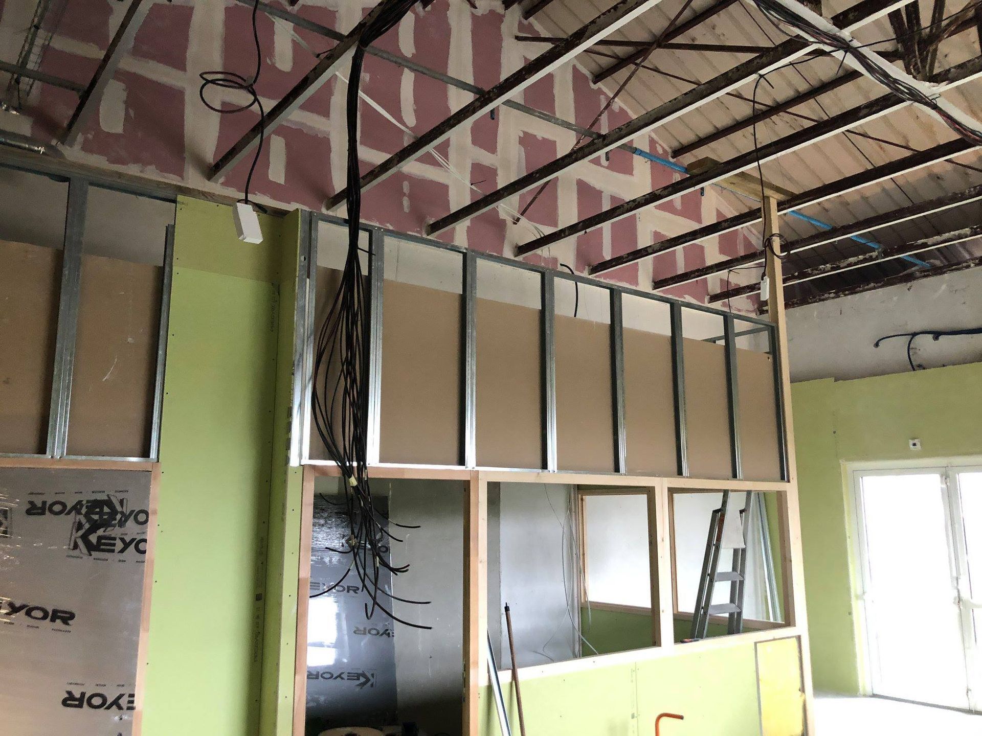 Ossature métallique partiellement recouverte de plaques de plâtre, câbles électriques et poutres apparentes.