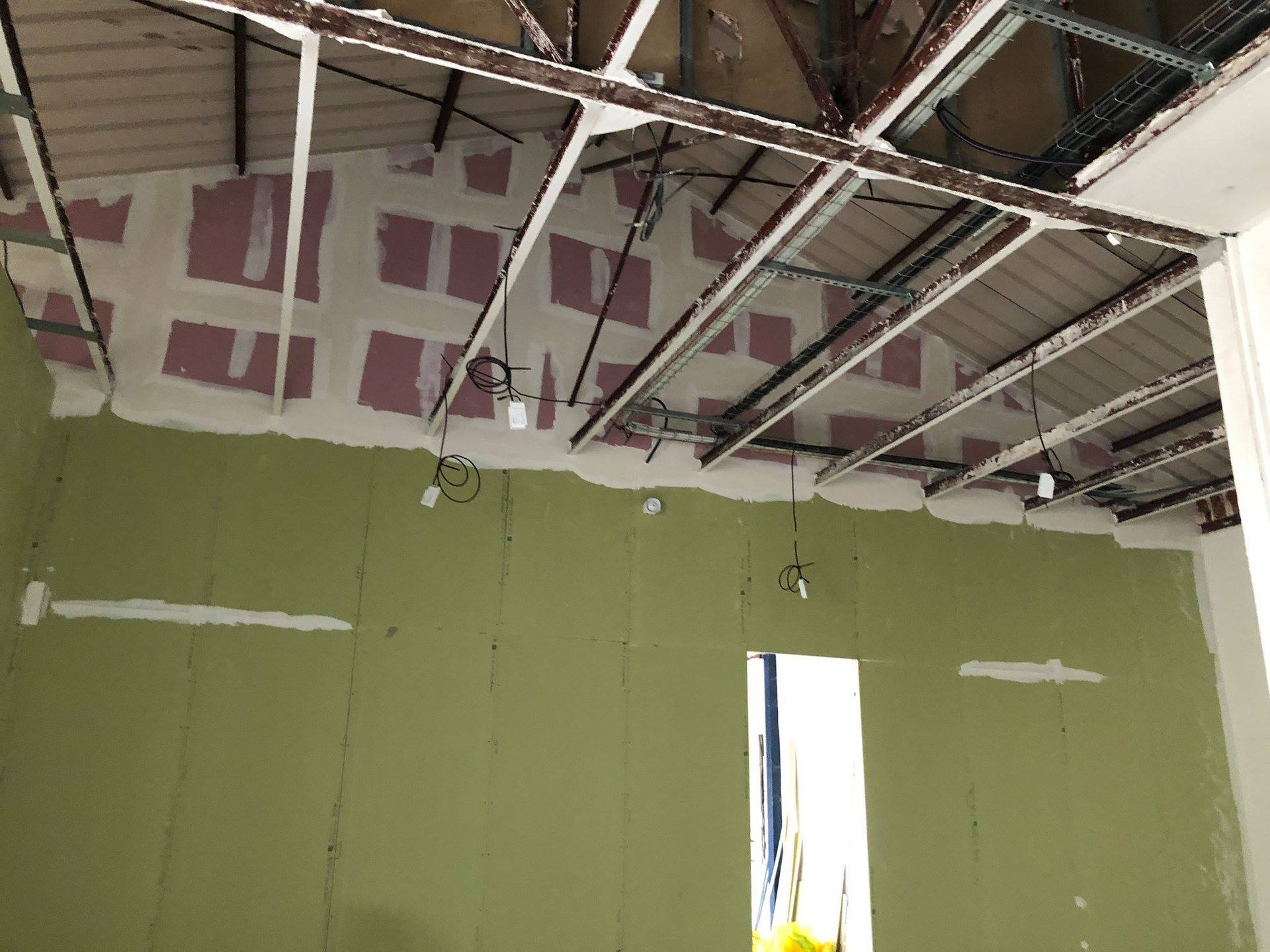 Intérieur d'un bâtiment en construction. Murs verts, charpente apparente, isolation rose visible.