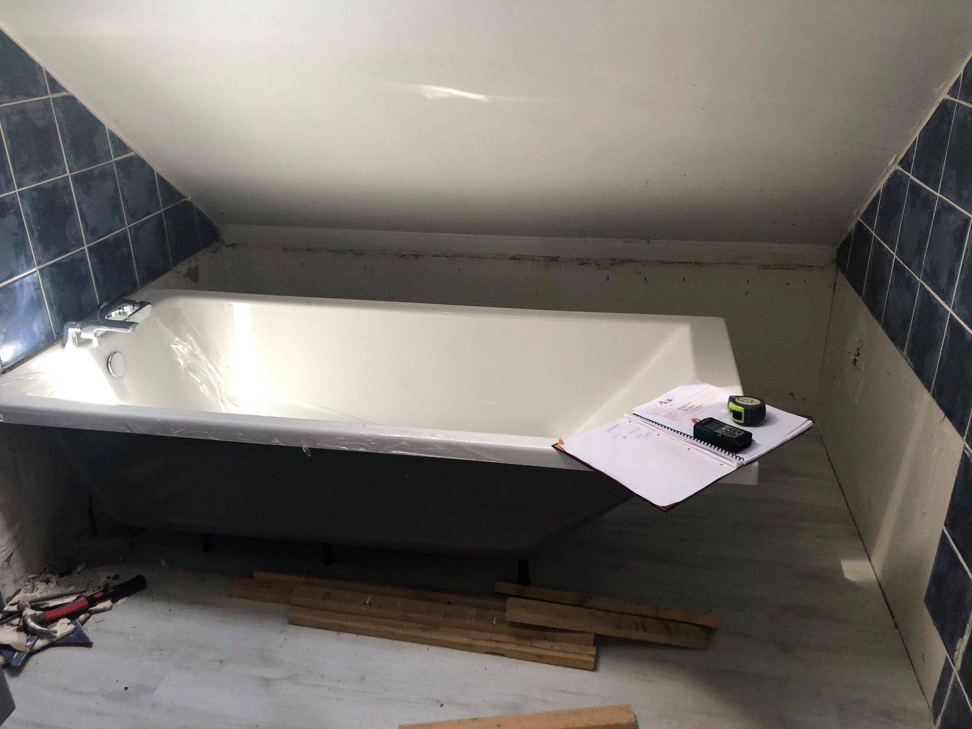 Salle de bains avec baignoire installée sous un plafond incliné, accents de carrelage bleu et matériaux de construction.