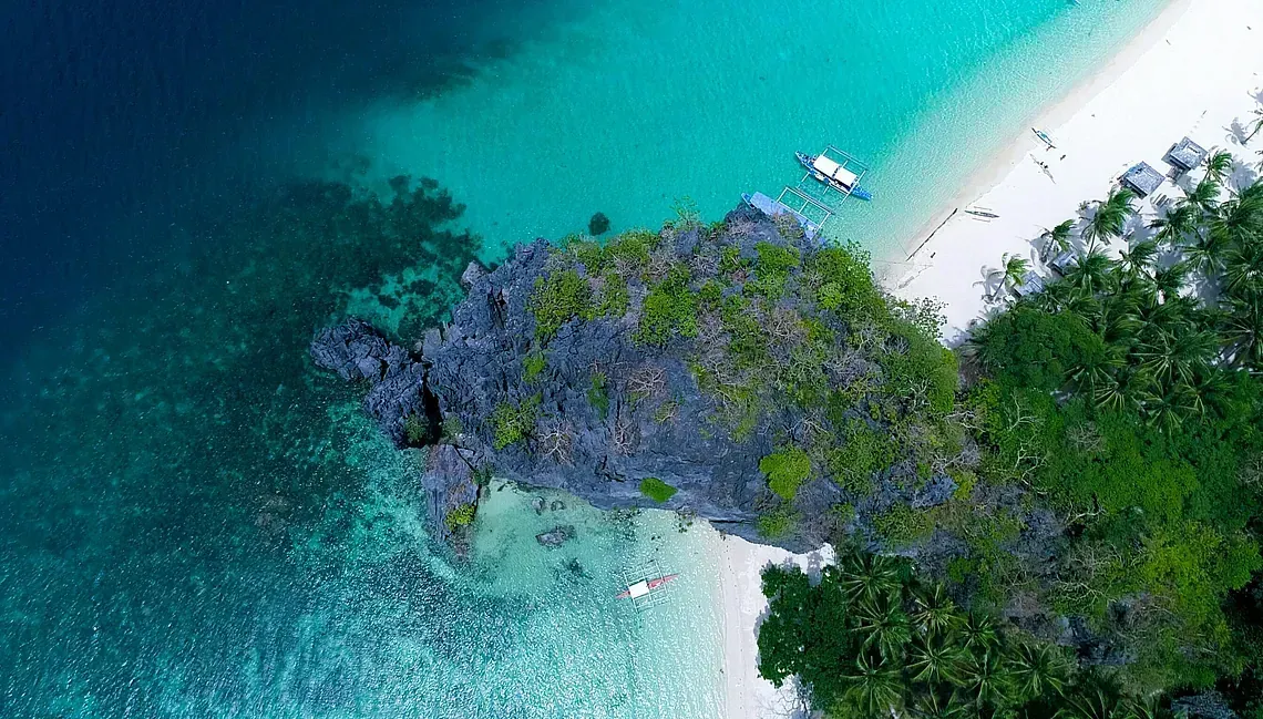 Una vista aérea de una playa tropical con un barco en el agua.