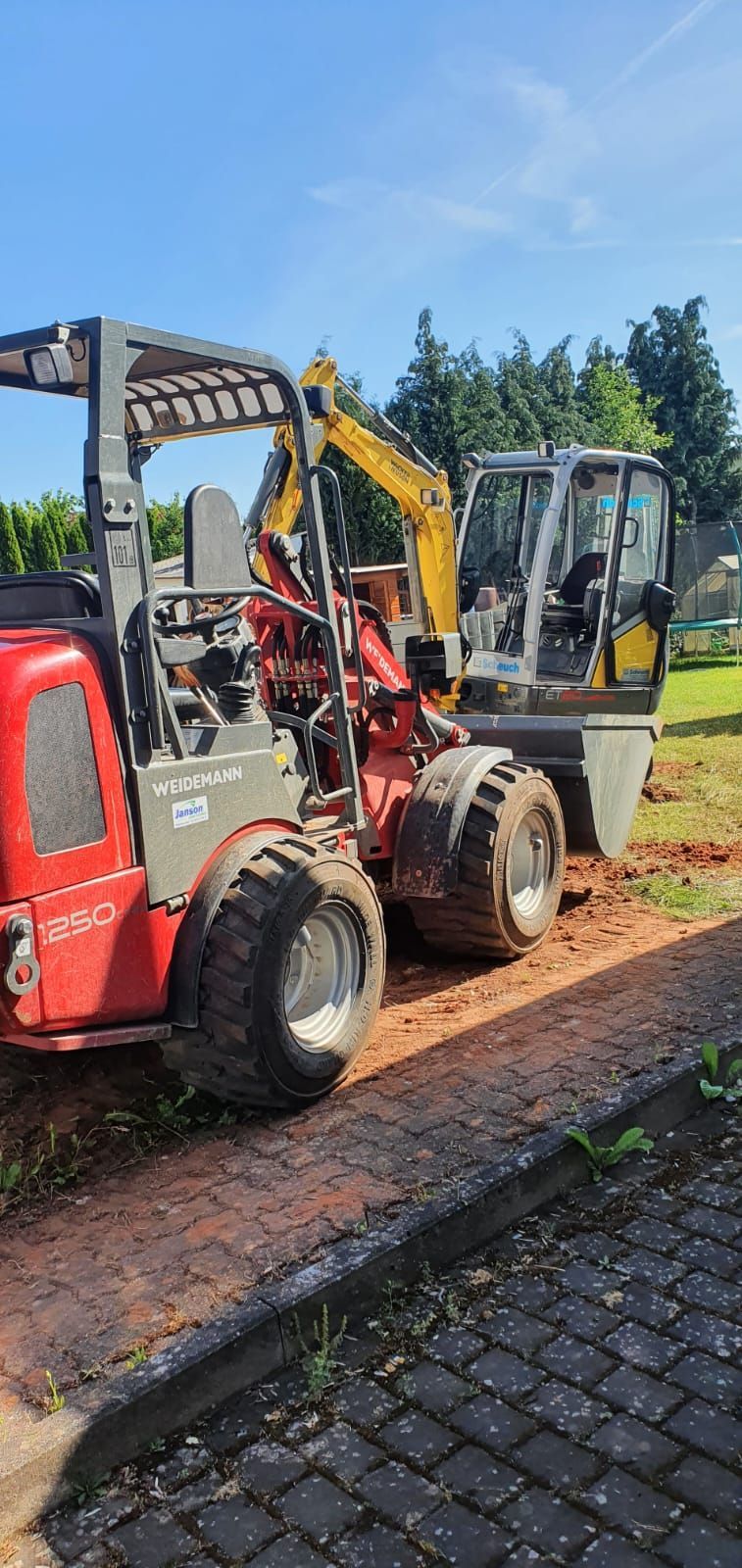 Ein roter Traktor und ein gelber Bagger stehen nebeneinander auf einem gepflasterten Gehweg.
