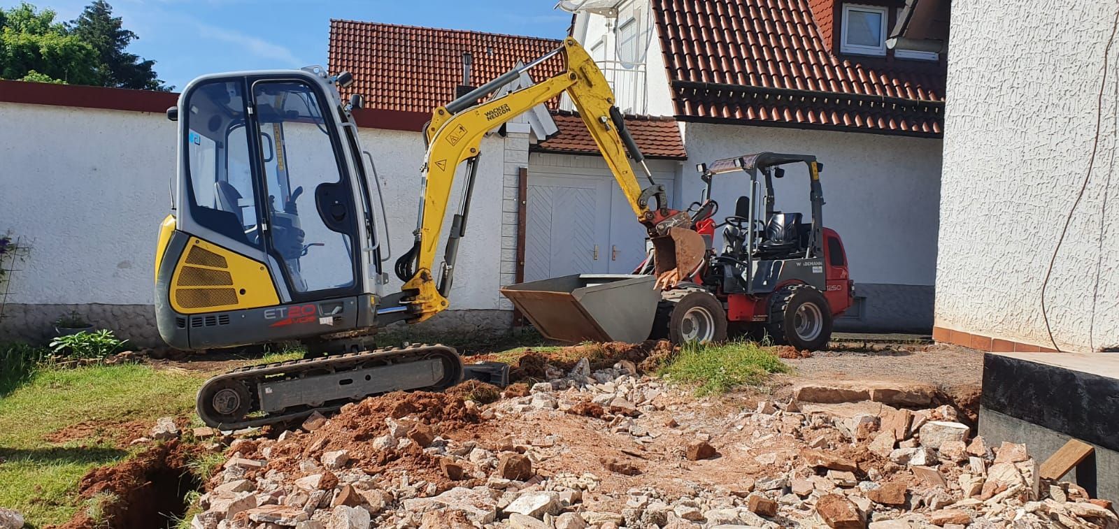 Ein gelber Bagger gräbt vor einem Gebäude ein Loch in den Boden.