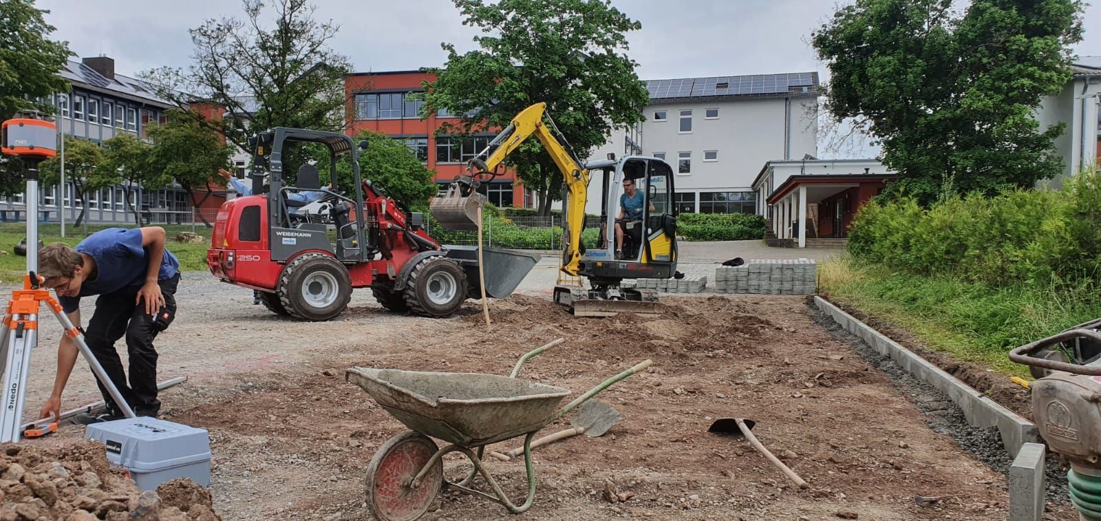 Ein Mann steht im Dreck neben einer Schubkarre und einem Traktor.