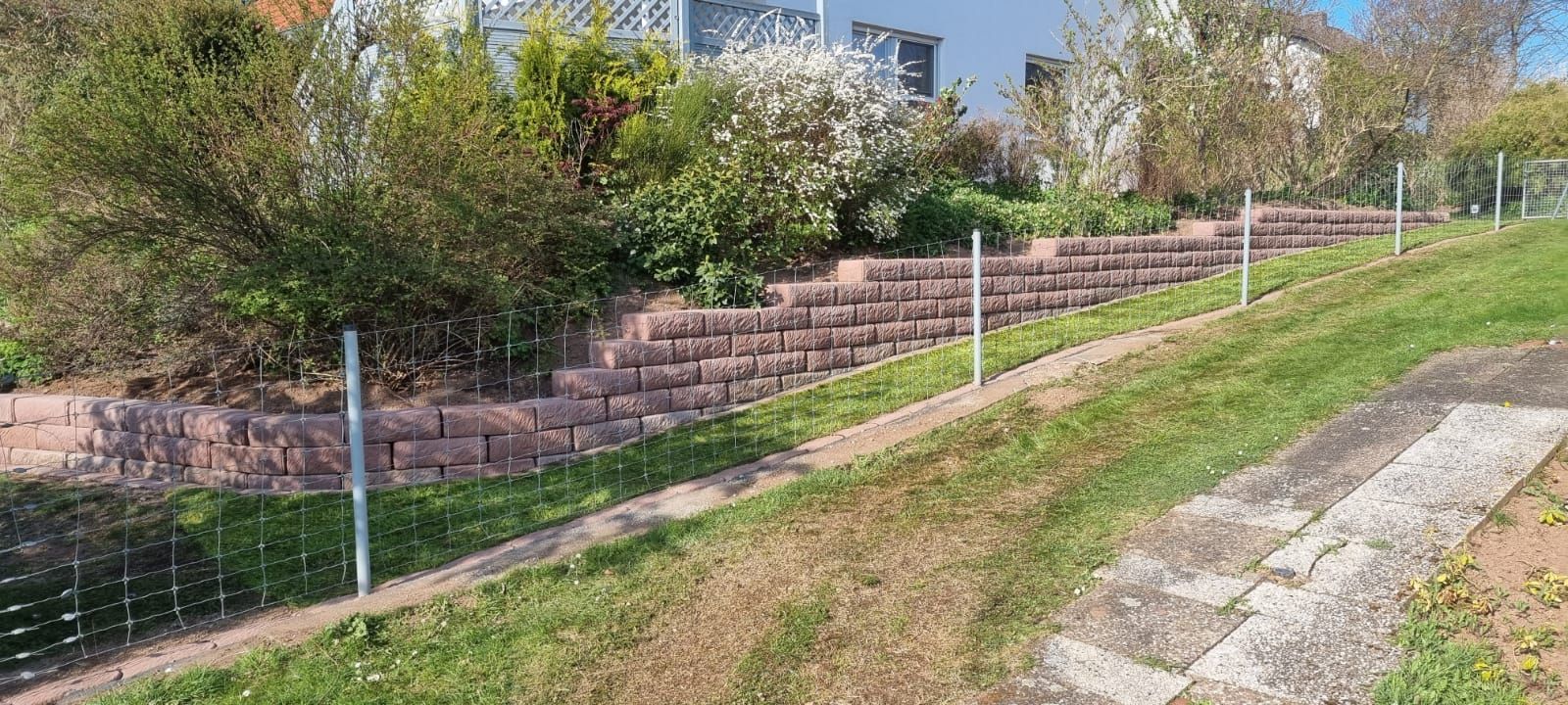 Ein Zaun umgibt einen grasbewachsenen Hügel mit einer Backsteinmauer im Hintergrund.