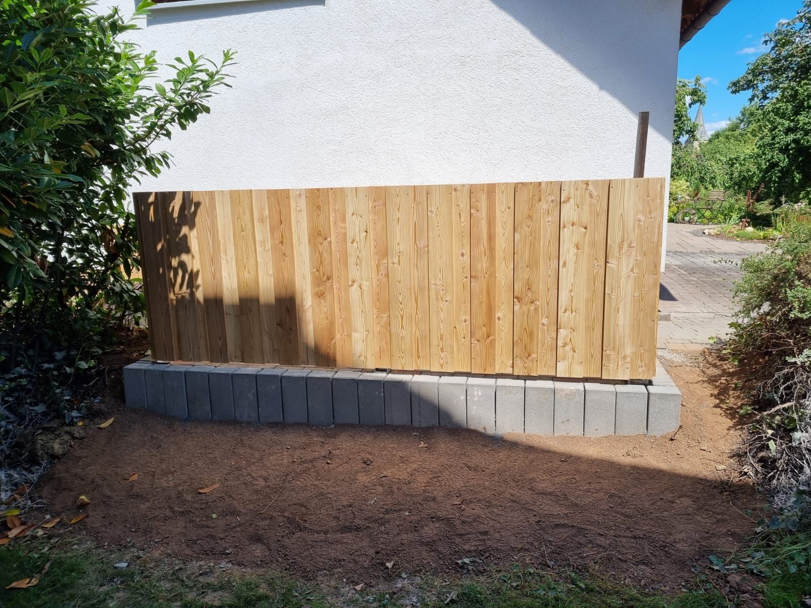 Vor einem weißen Gebäude steht ein Holzzaun.