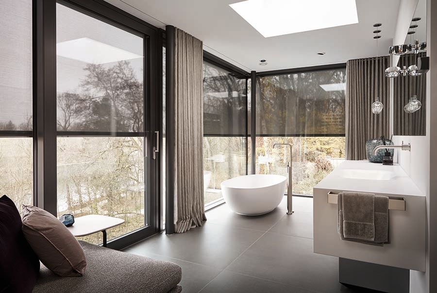 Weißer Fenstergriff an einem offenen Fenster, draußen blauer Himmel und grüne Bäume.