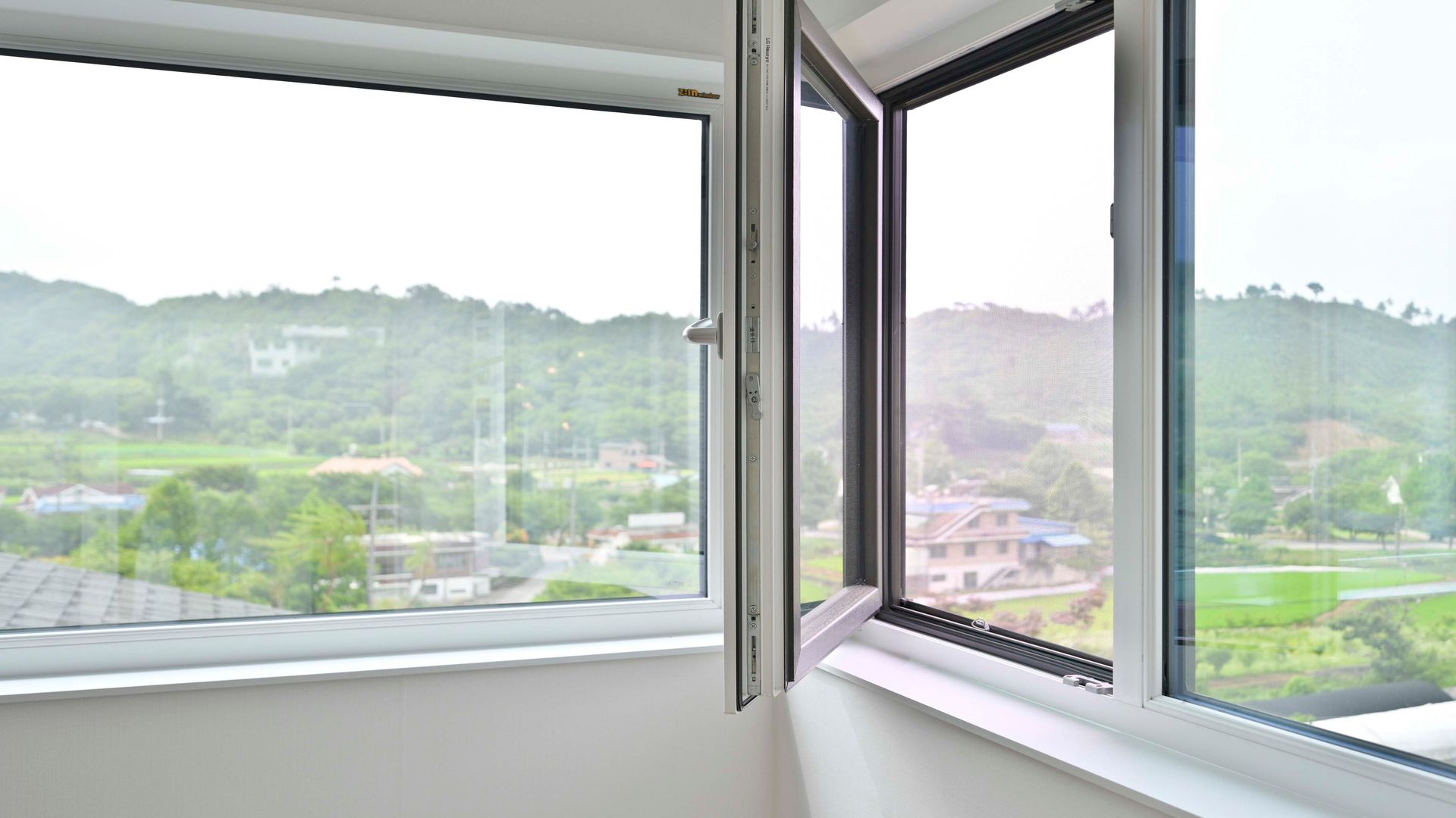 Offenes Fenster mit Blick auf einen grünen Hügel und die Dächer an einem nebligen Tag
