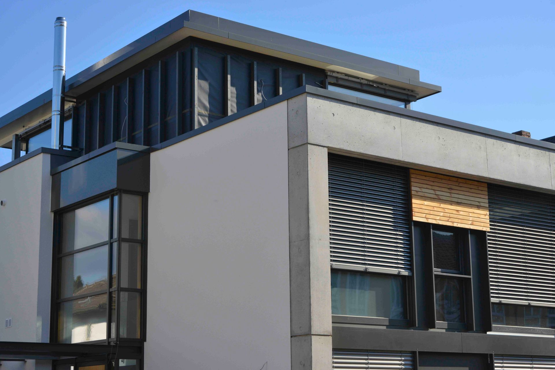 Modernes Gebäudeäußeres mit weißen Wänden, dunklen Fenstern und blauem Himmel darüber