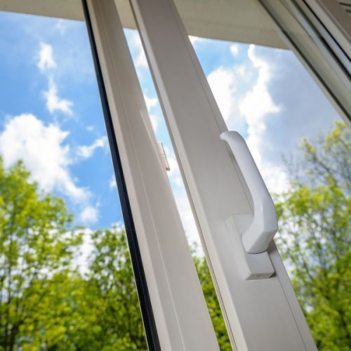 Ein weißes Fenster mit Griff und Blick auf Bäume