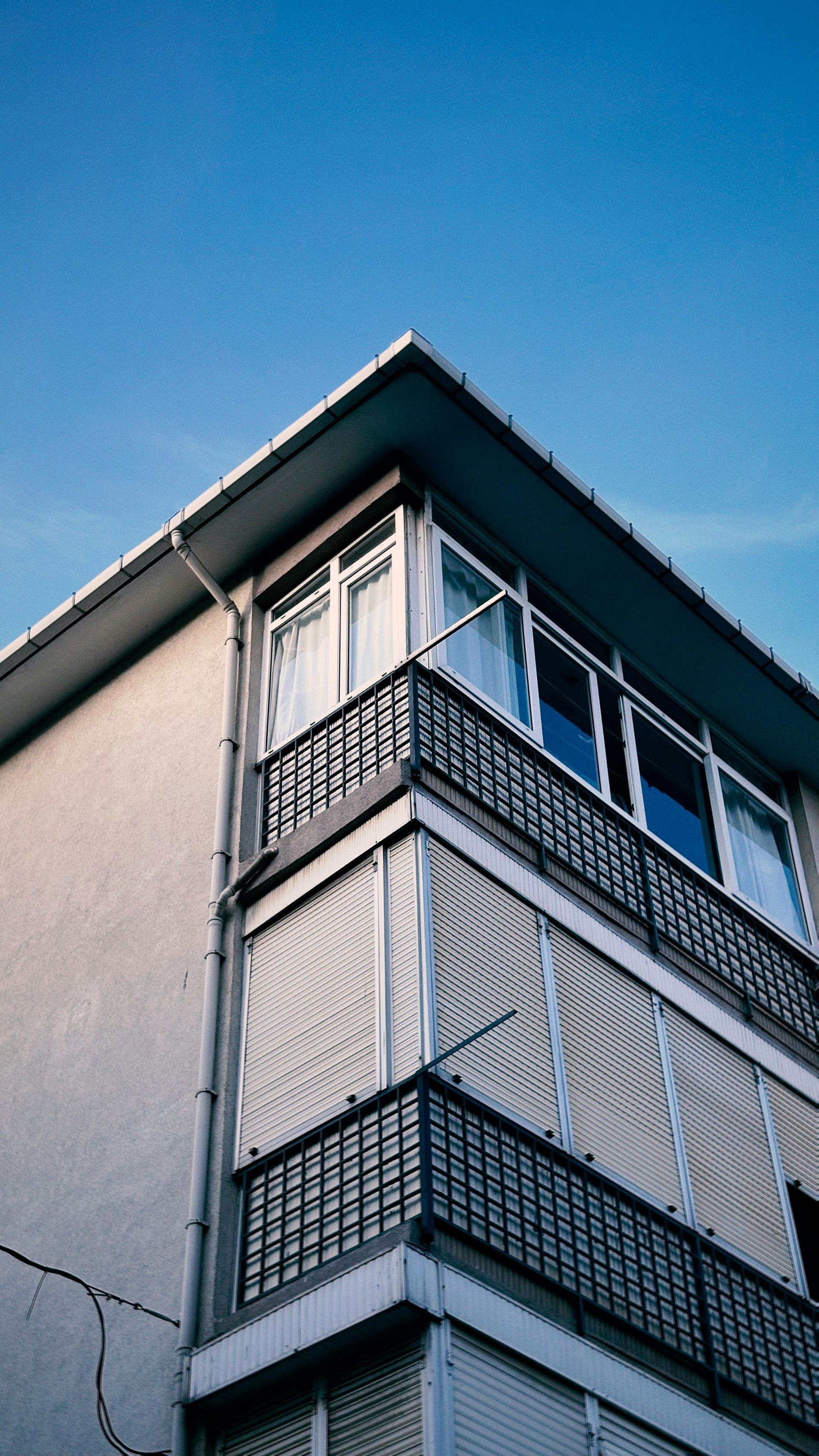 Ecke eines weißen Wohnhauses mit Balkonen vor einem klaren blauen Himmel