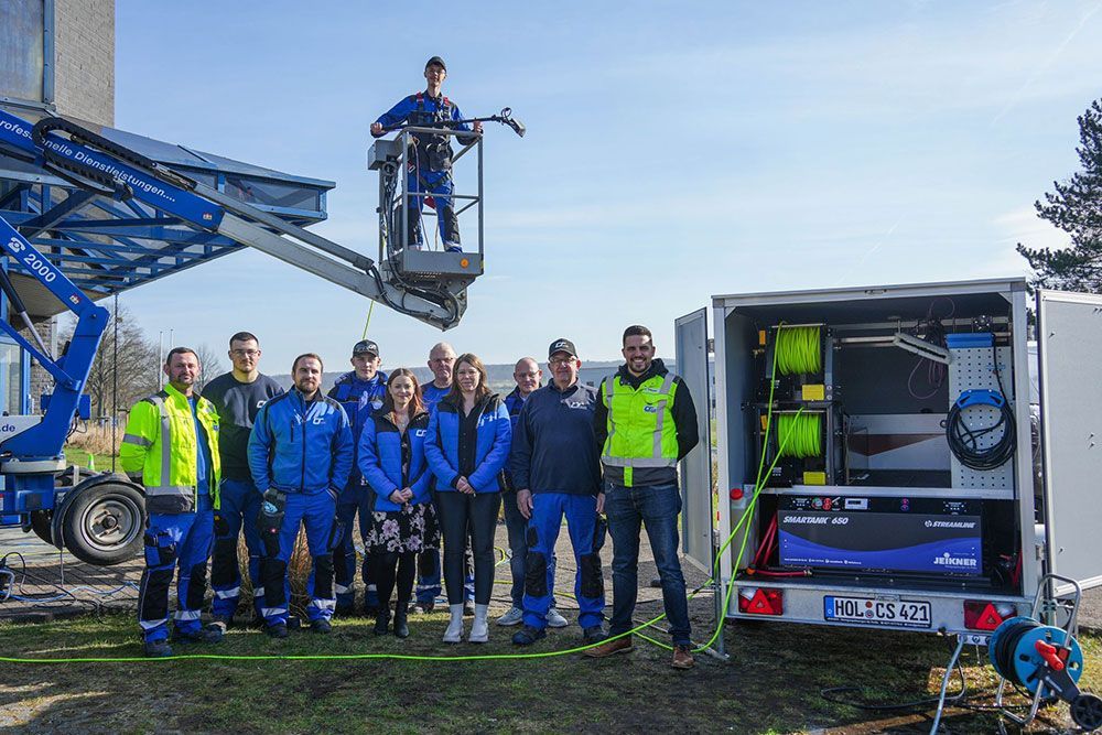 Eine Gruppe von Menschen posiert vor einem Kran für ein Foto.