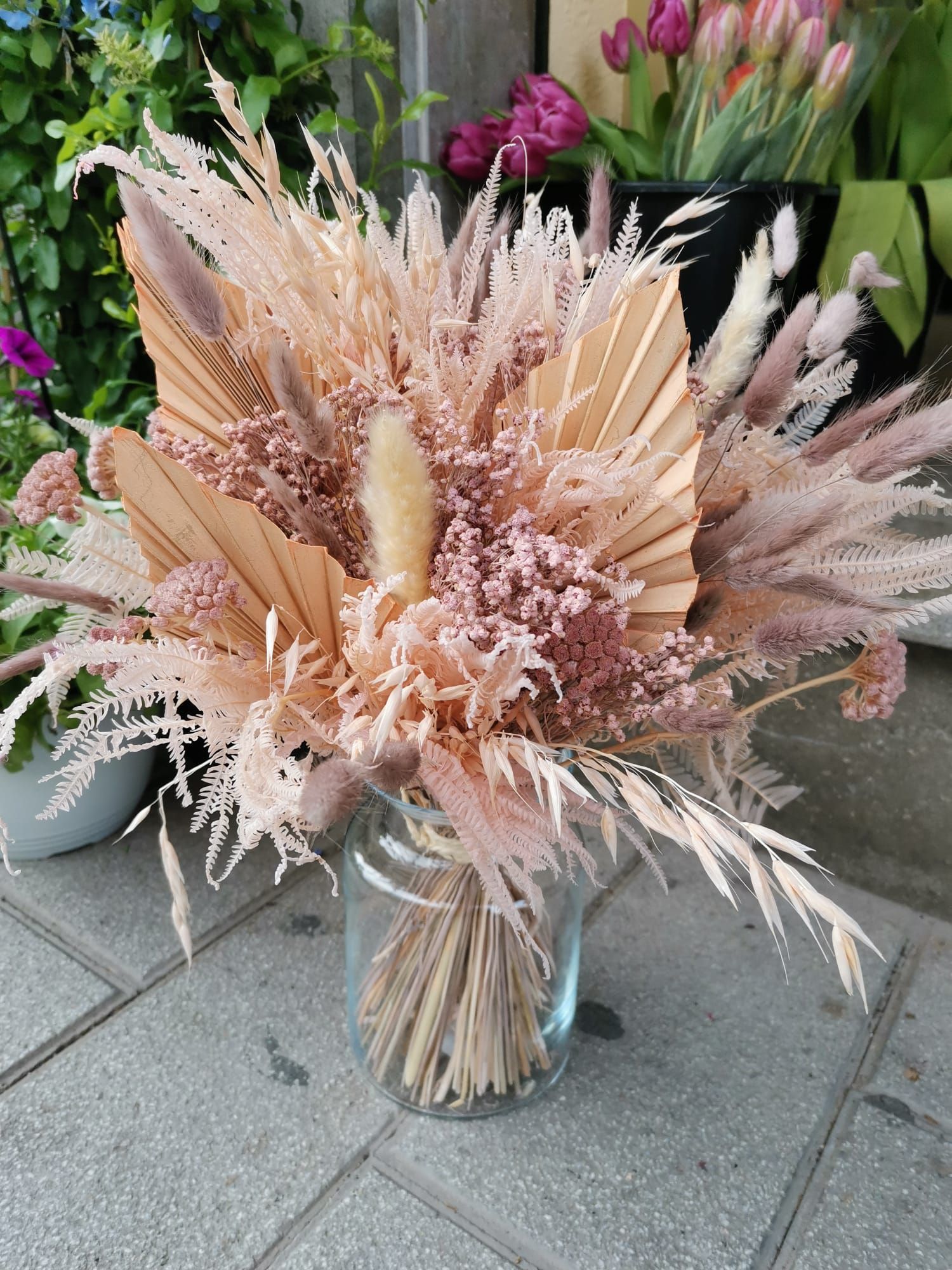 Un jarrón lleno de flores secas está sobre una acera.