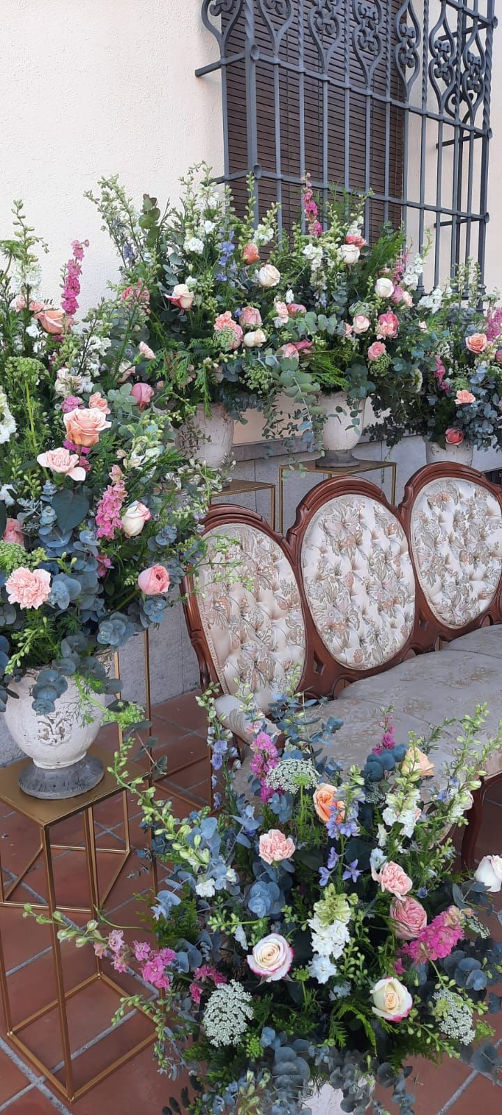 Un sofá está rodeado de jarrones llenos de flores.