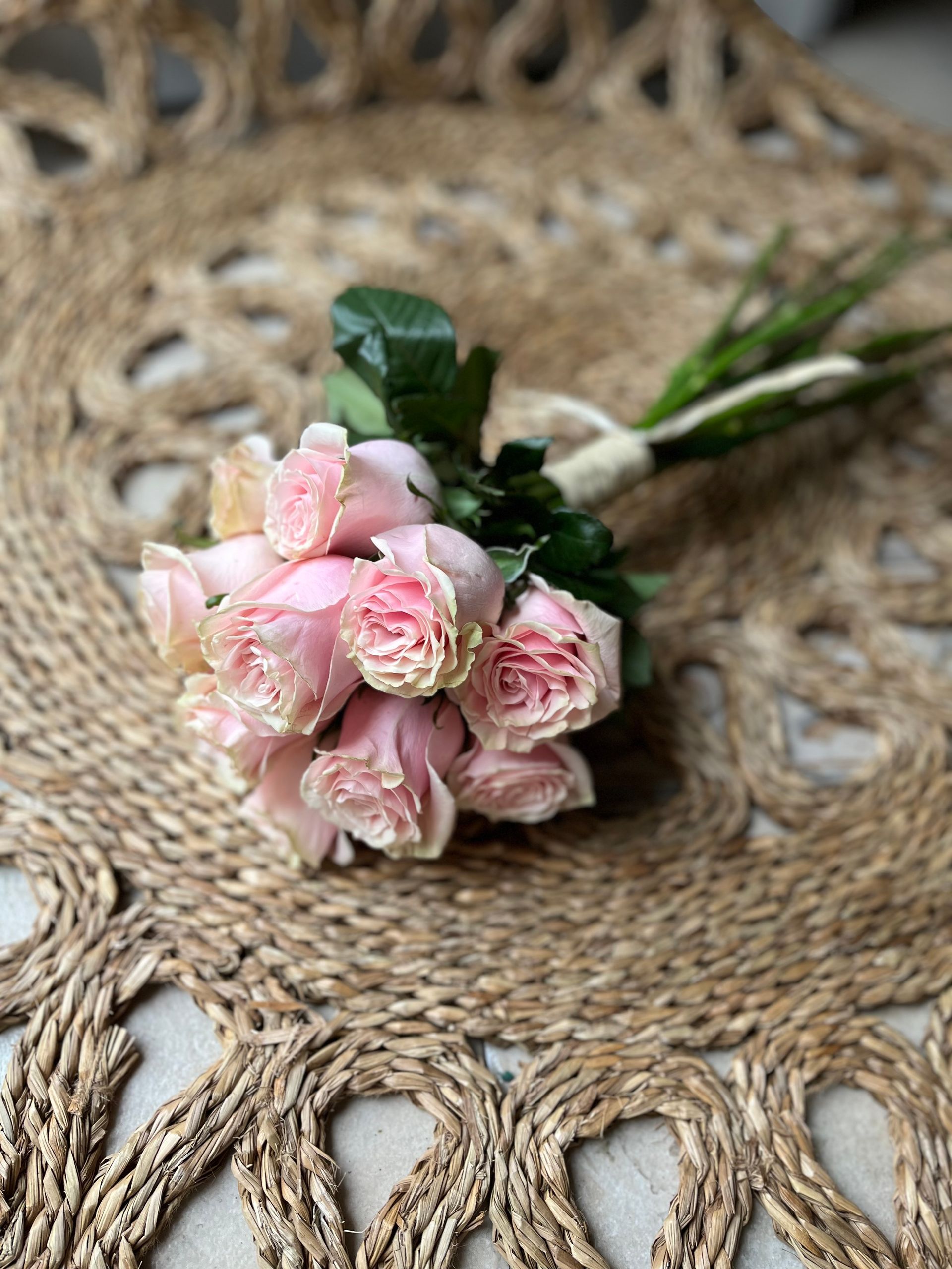 Un ramo de rosas rosadas reposa sobre una alfombra de yute.