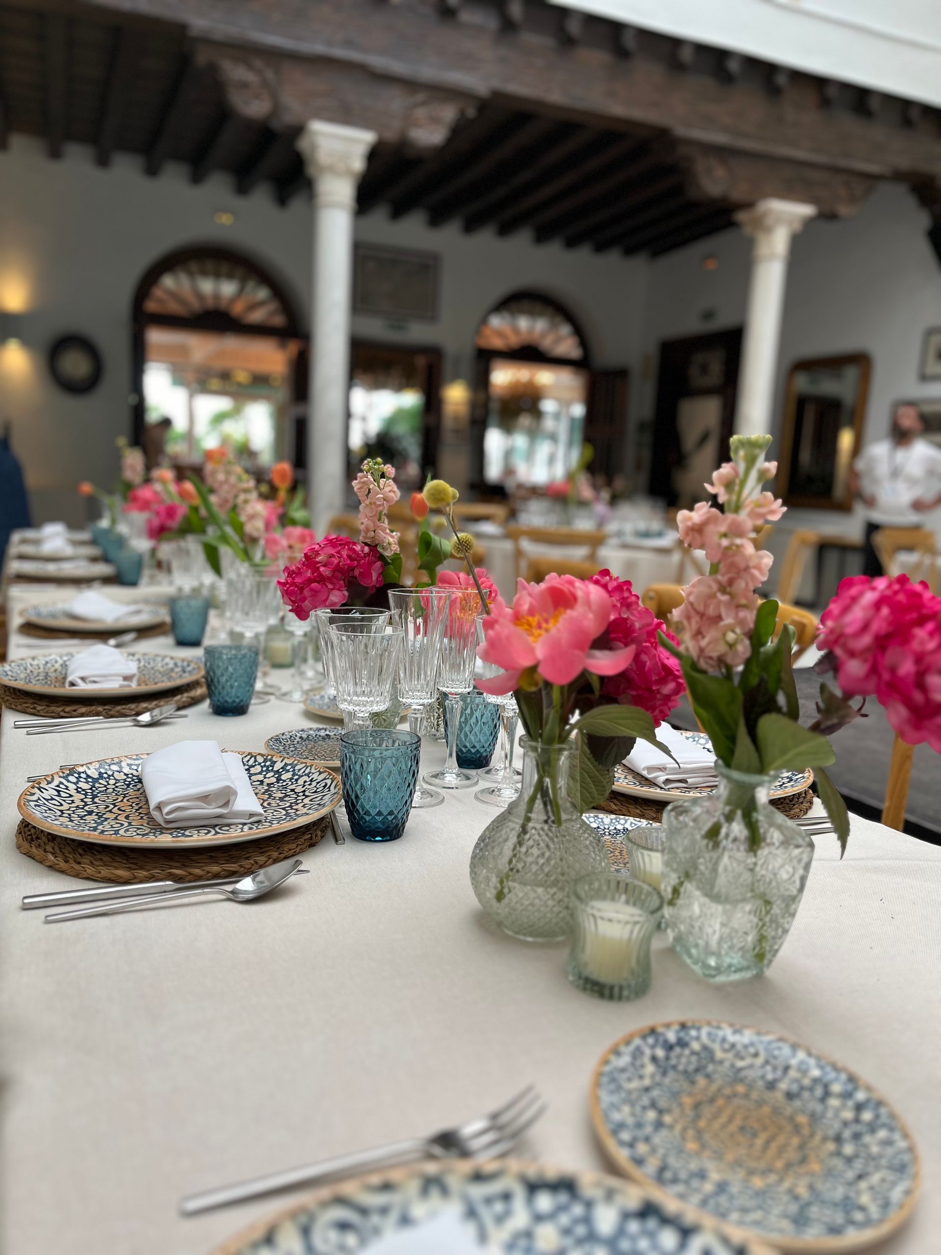 Una mesa con platos, vasos, jarrones y flores sobre ella.