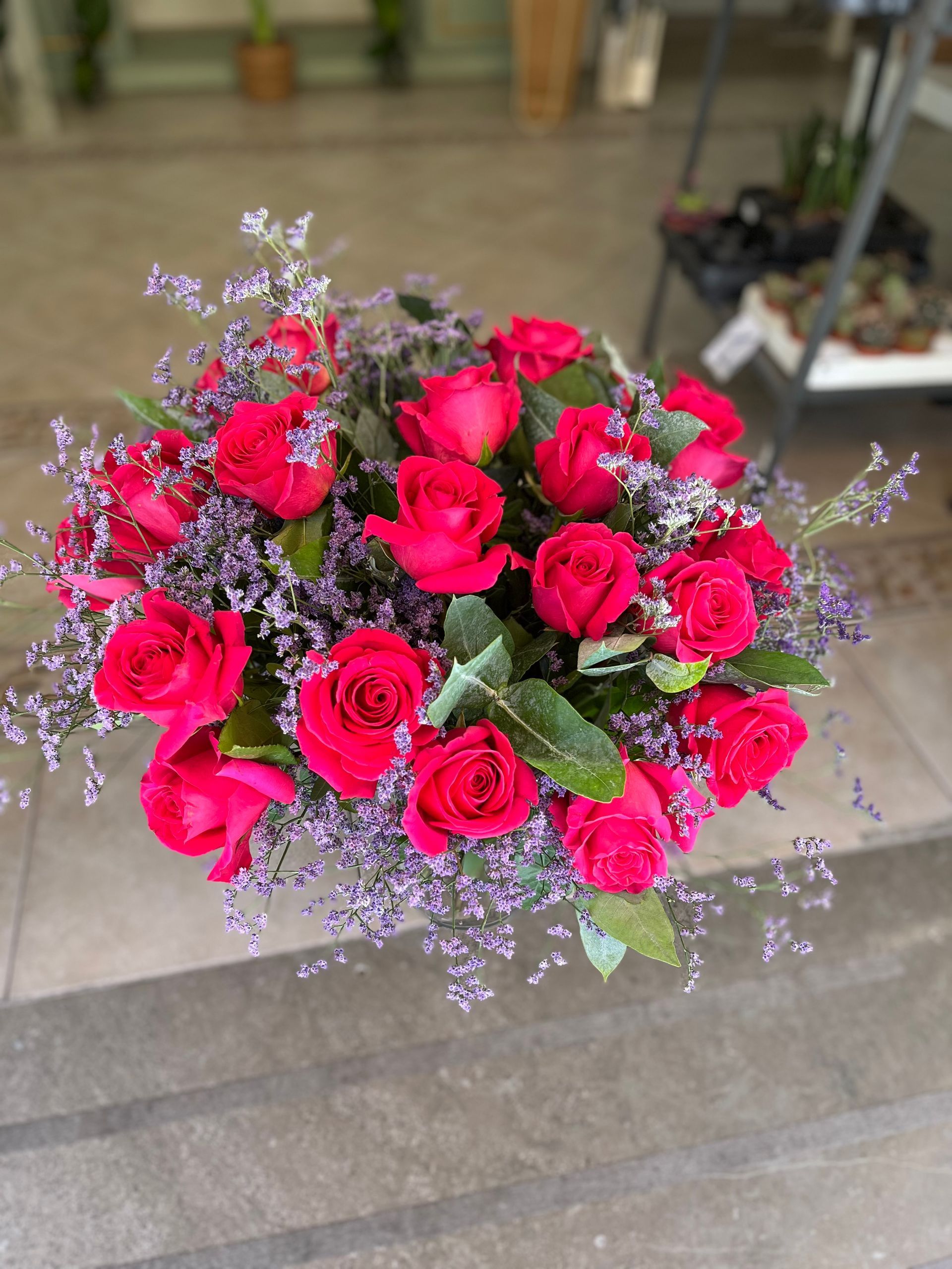 Un ramo de rosas rojas y flores violetas se encuentra sobre un suelo de baldosas.