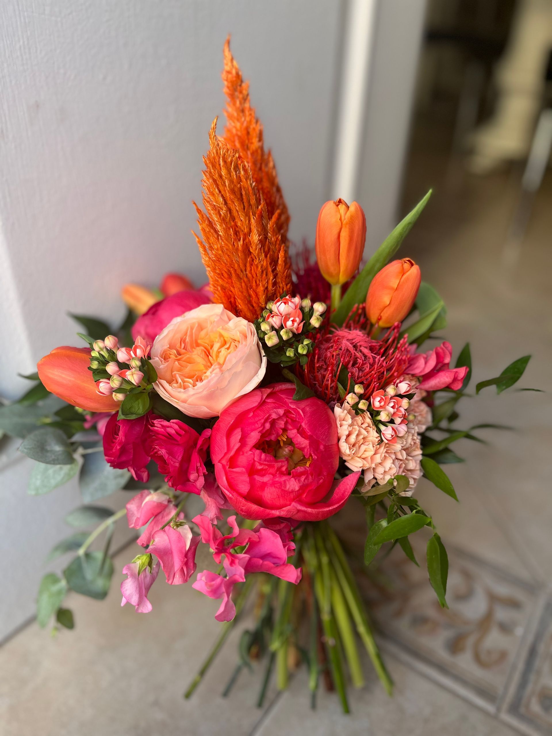 Un ramo de flores rosas y naranjas está sobre un suelo de baldosas.