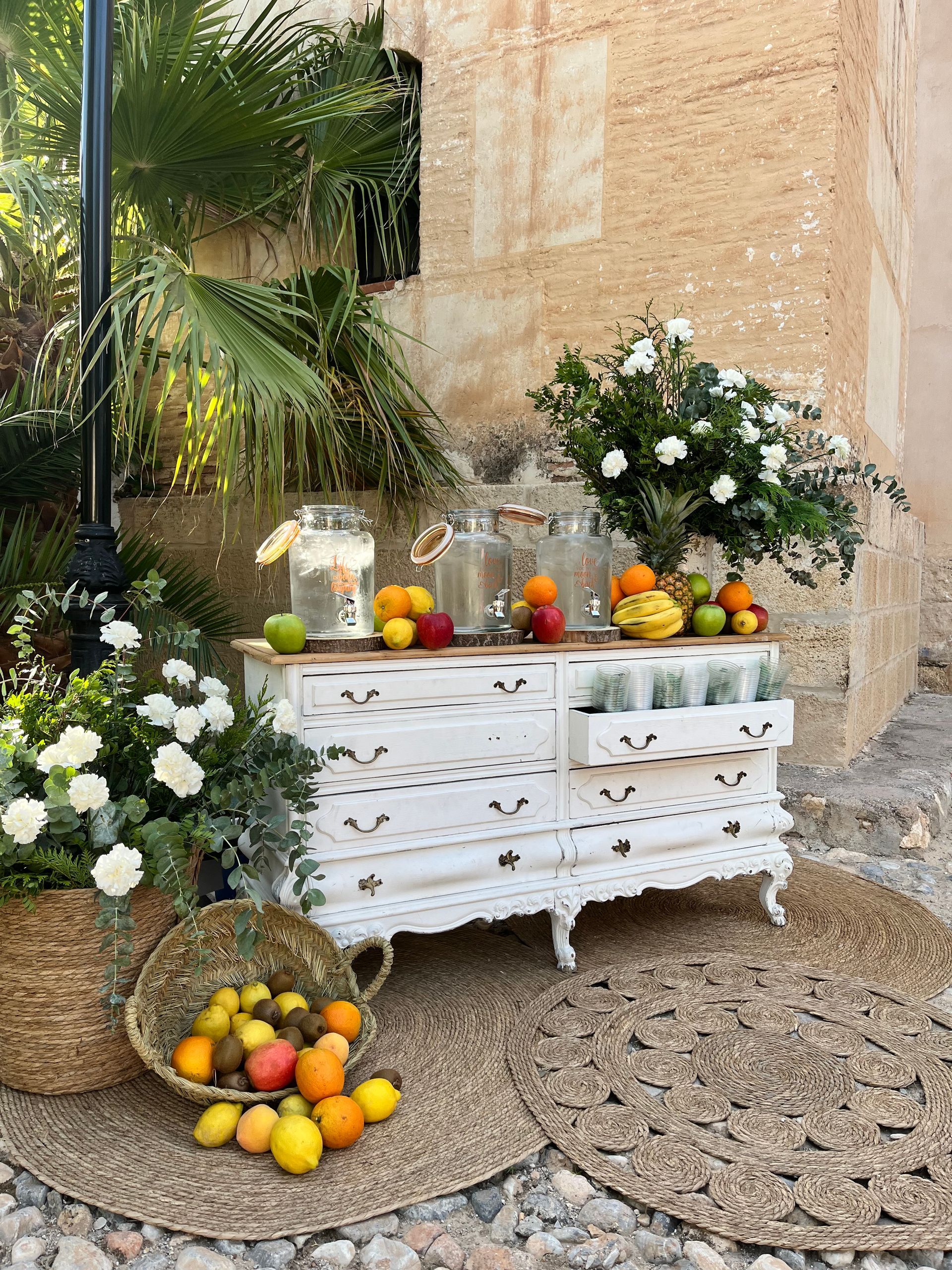 Un tocador blanco lleno de frutas y flores se encuentra frente a un edificio.