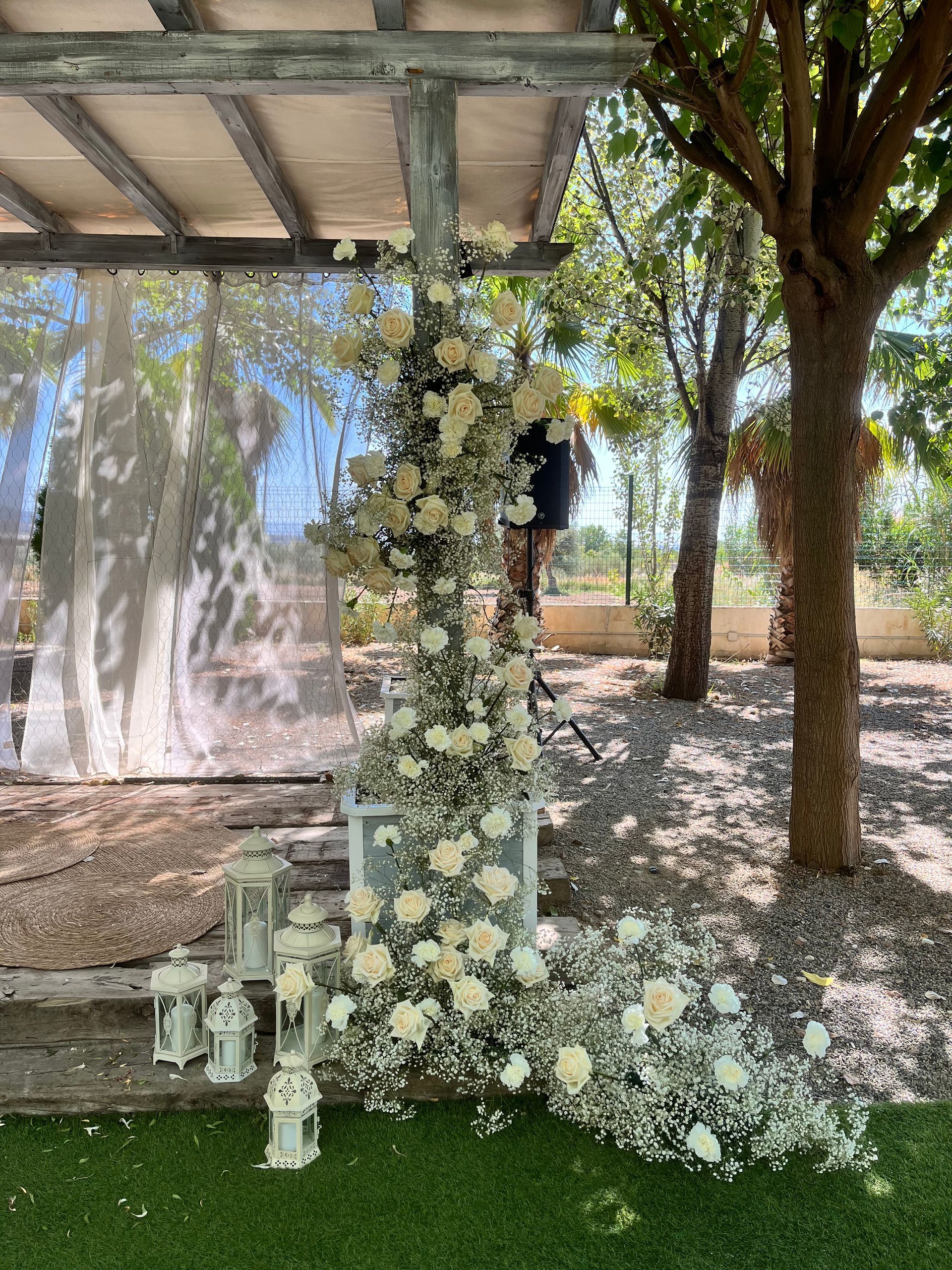 Una persona está parada debajo de una pérgola decorada con flores blancas y flores de bebé.