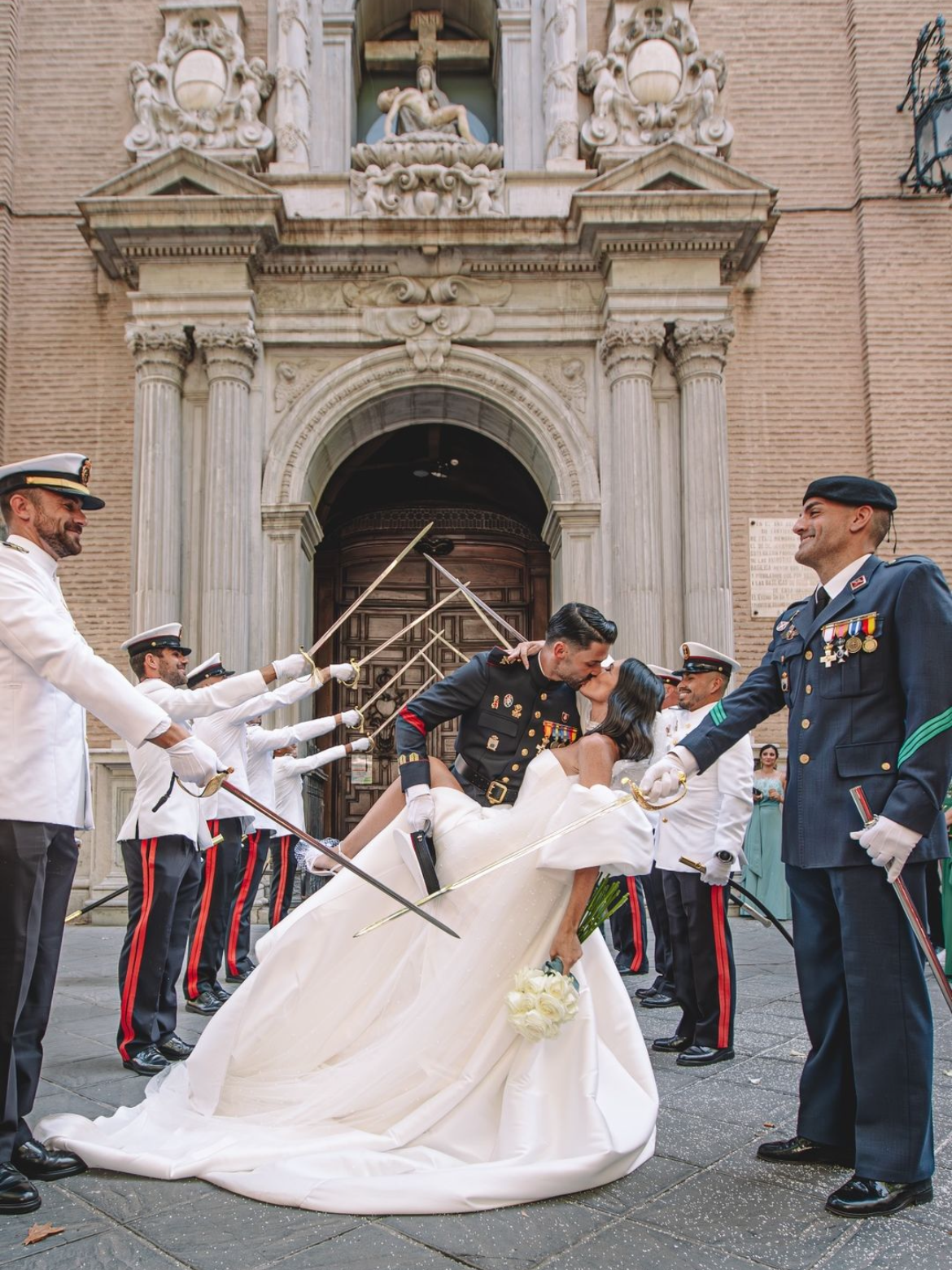 Una novia y un novio besándose frente a una iglesia con soldados sosteniendo espadas.