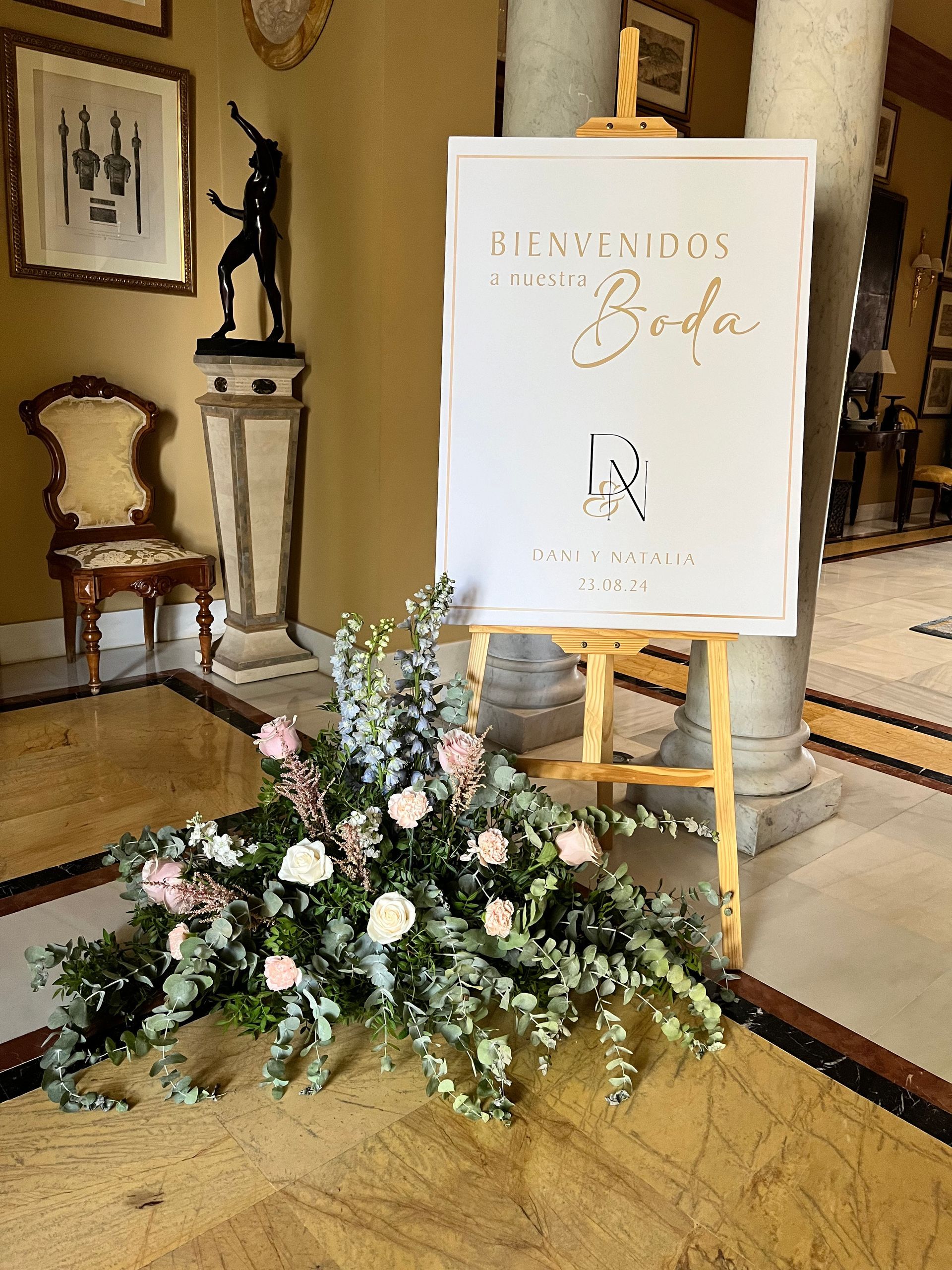 Un cartel en un caballete con flores delante.