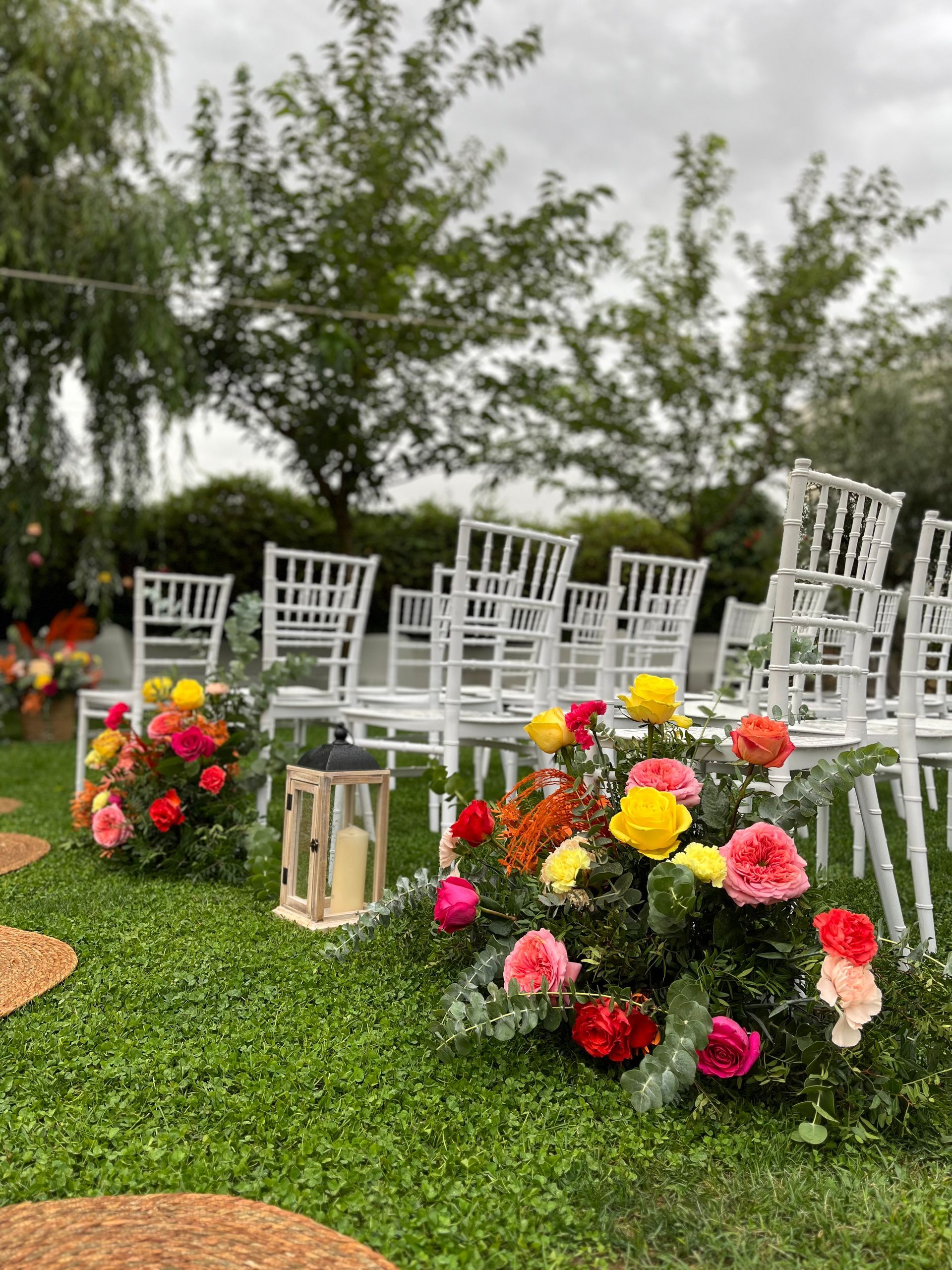 Una fila de sillas blancas colocadas sobre un exuberante campo verde rodeado de flores de colores.