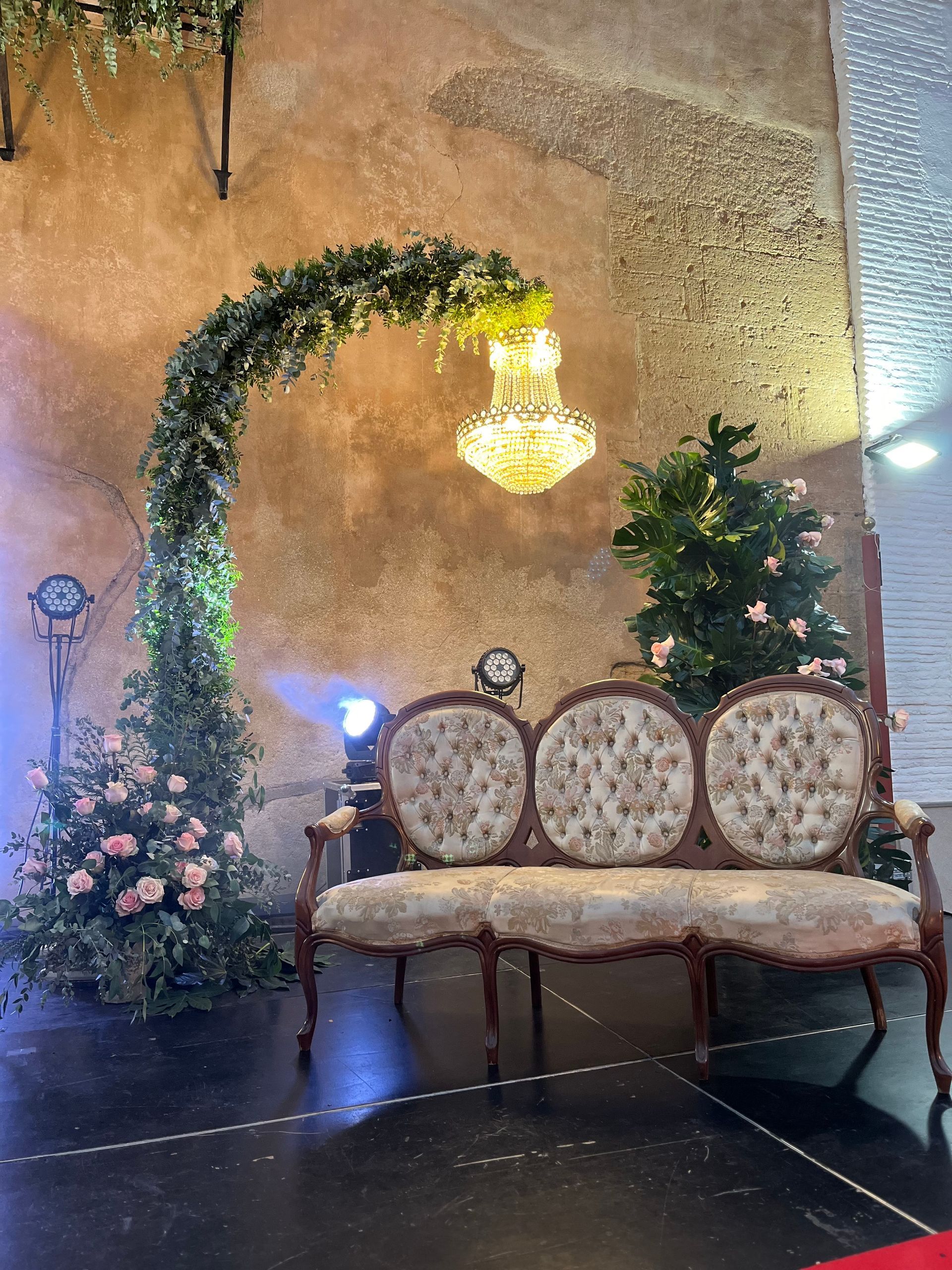 Un sofá está sentado frente a una pared con flores y una lámpara de araña.