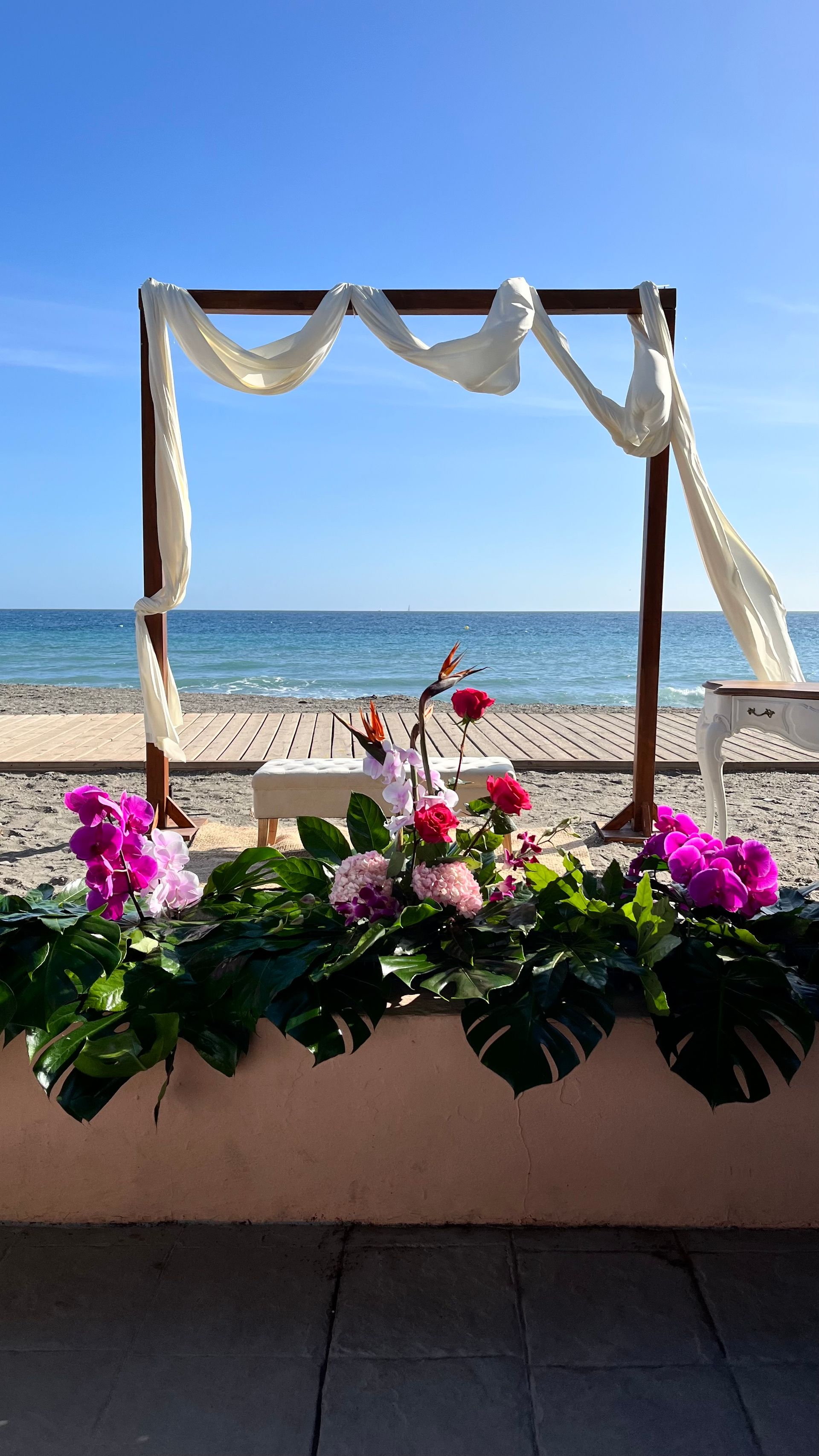 Un arco de boda en la playa con flores y vista al océano.