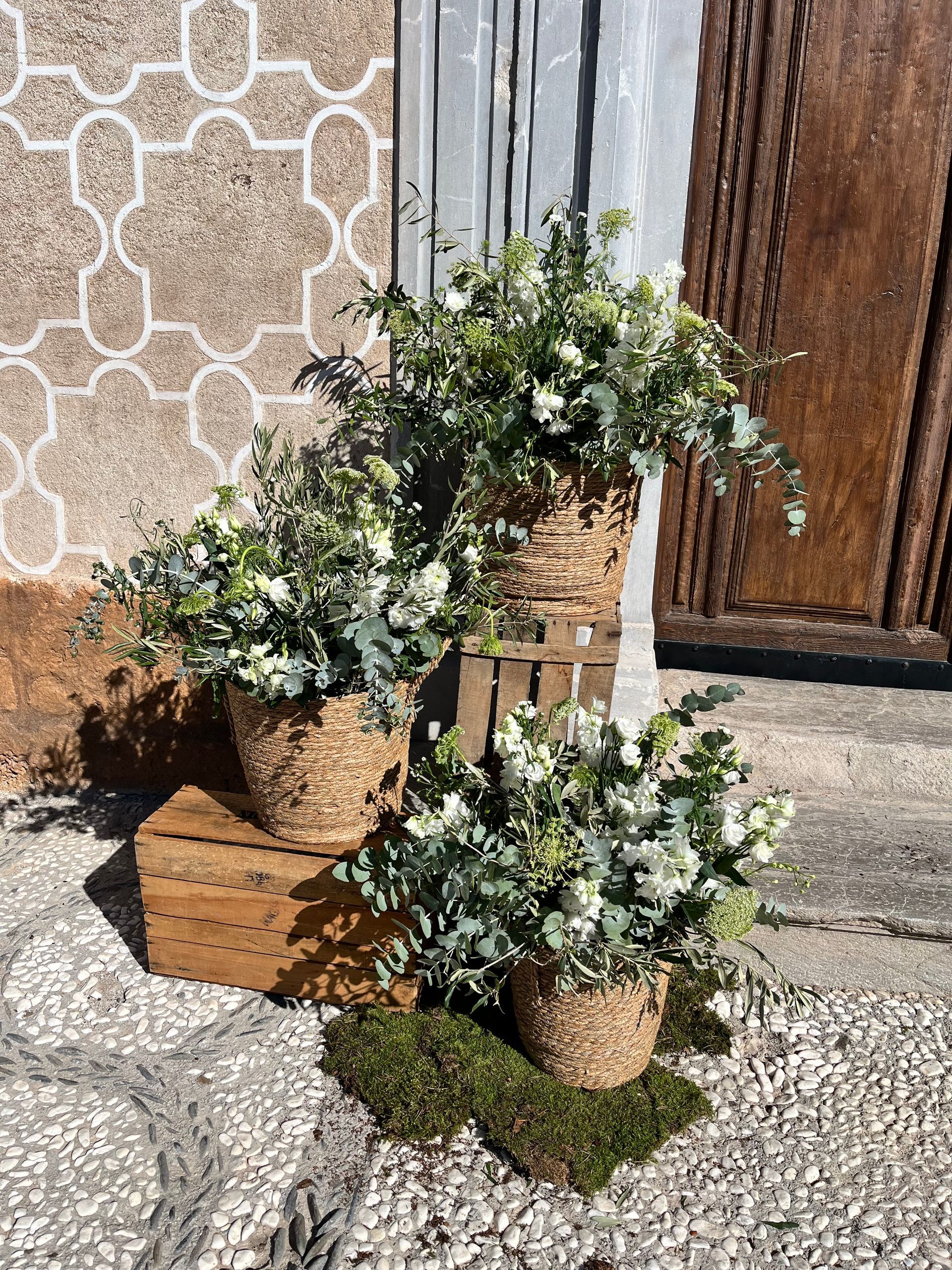 Tres cestas llenas de flores están colocadas encima de una caja de madera.