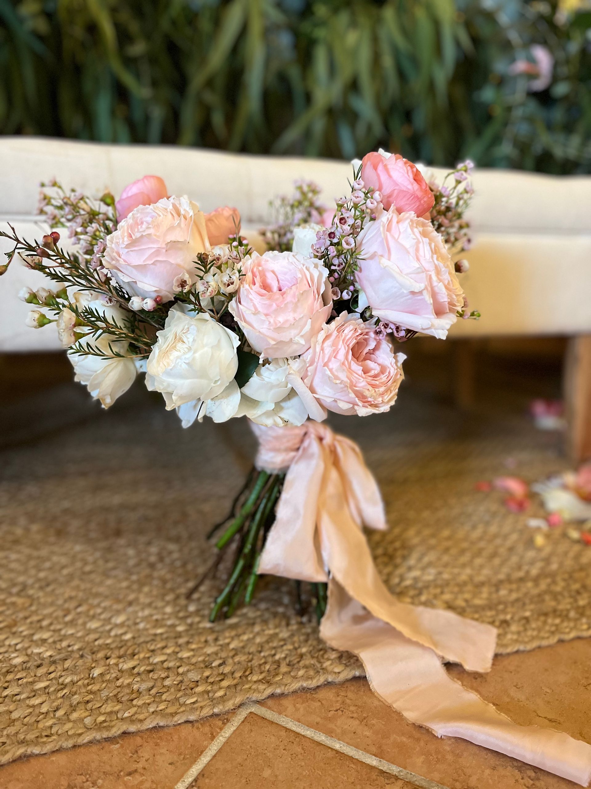 Un ramo de flores rosas y blancas con una cinta rosa está sobre una alfombra.