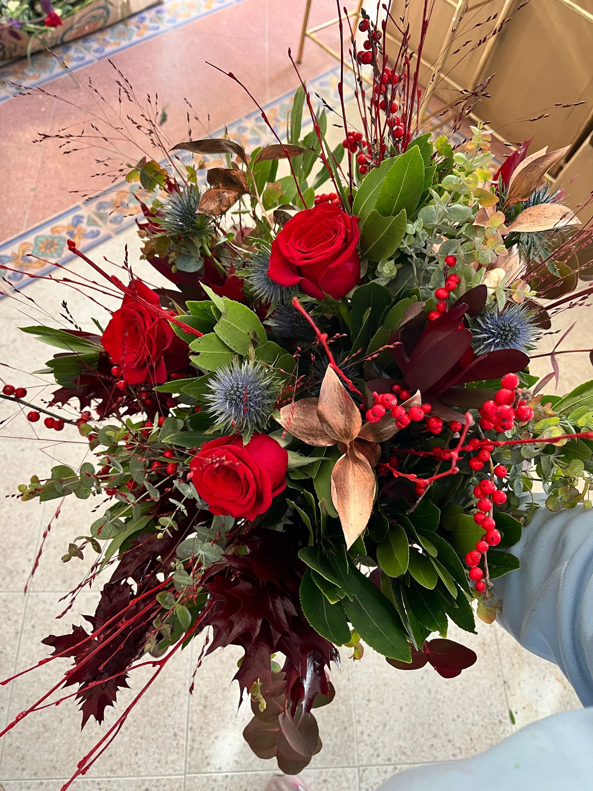 Una persona sostiene un ramo de rosas rojas y bayas.